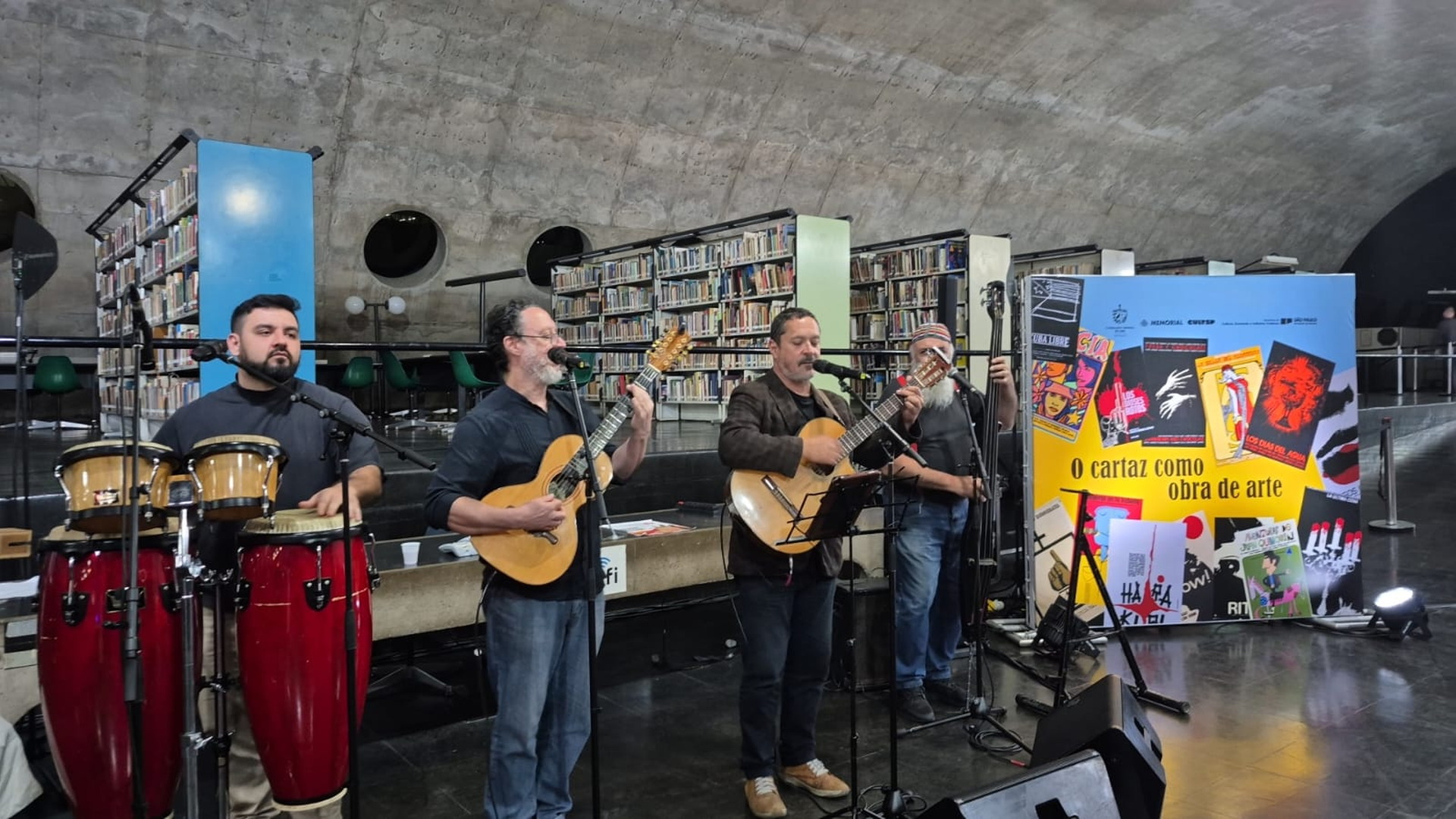 Grupo musical se presenta con instrumentos de percusión y cuerda ante un panel colorido