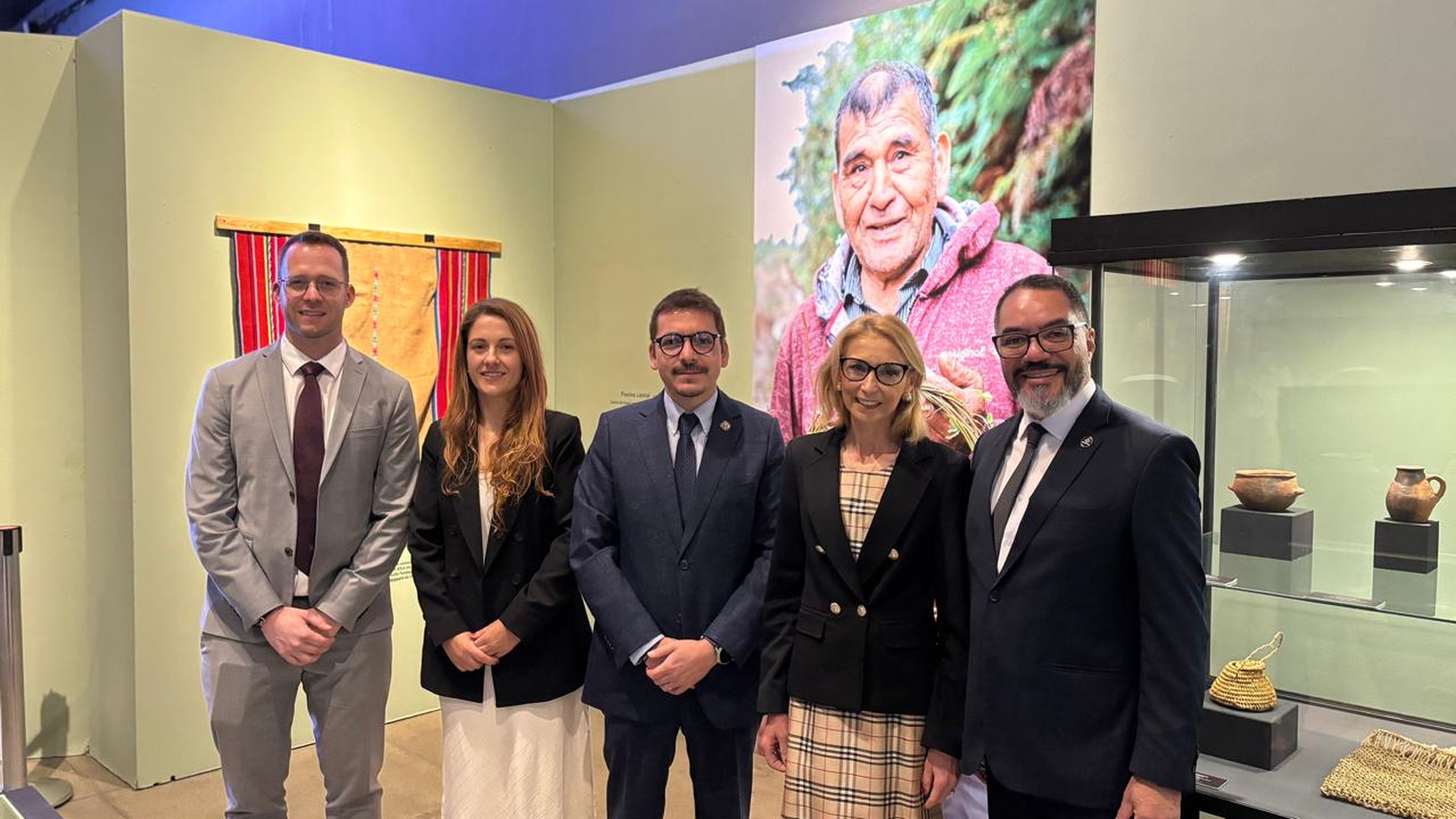 João Carlos Corrêa y cuatro invitados posan ante paneles expositivos rojos y piezas museológicas