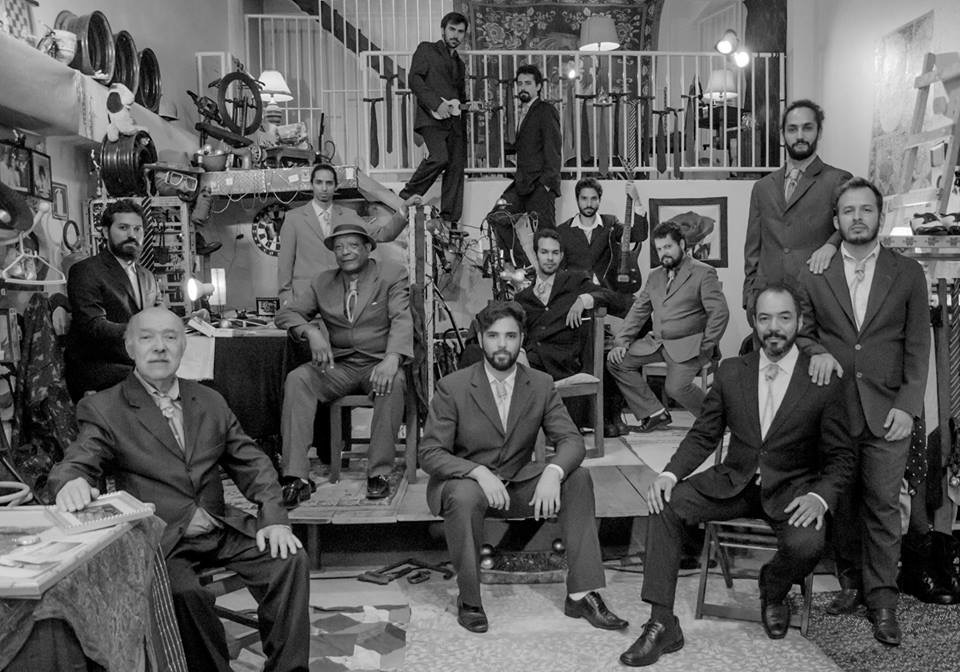 Elenco masculino distribuído em diferentes planos de um ambiente cenográfico, em fotografia em preto e branco