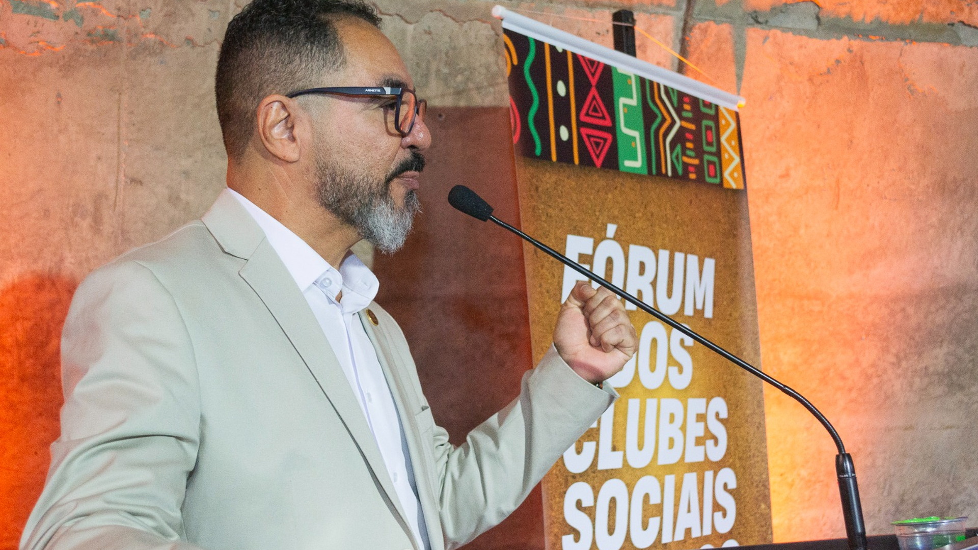 João Carlos Corrêa habla al micrófono durante un foro sobre clubes sociales, ante un panel del evento