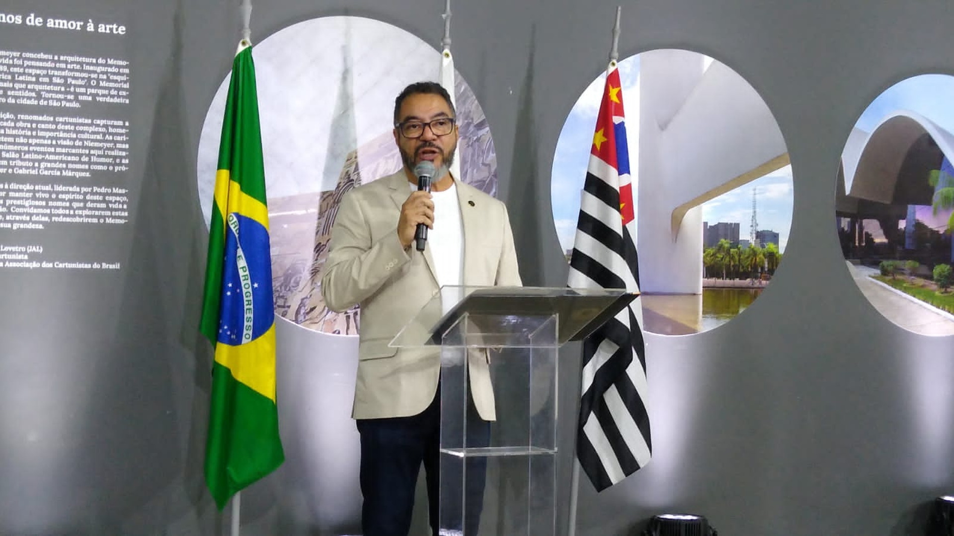 João Carlos Corrêa habla en el atril, con banderas al fondo y la escultura conmemorativa de los 35 años en primer plano