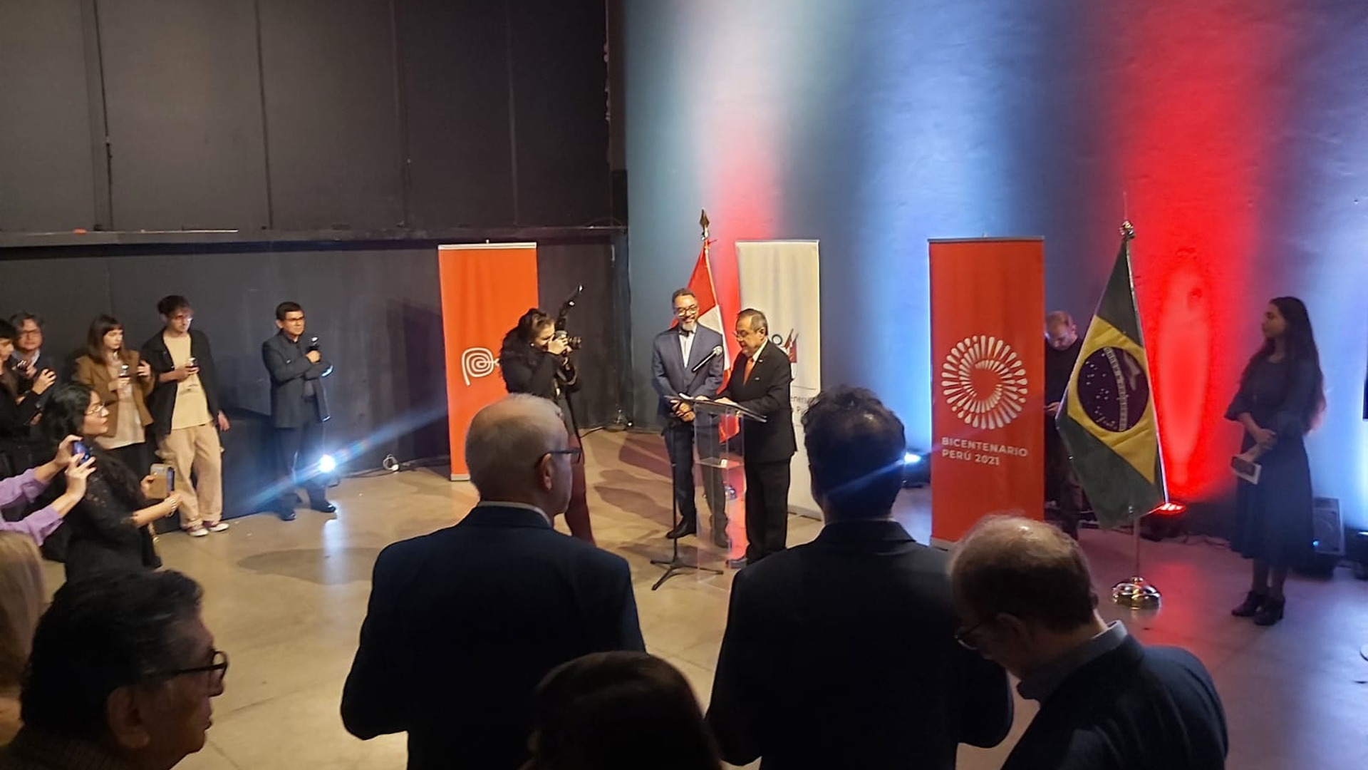 Presentación escénica en un espacio expositivo iluminado en rojo, ante un público sentado