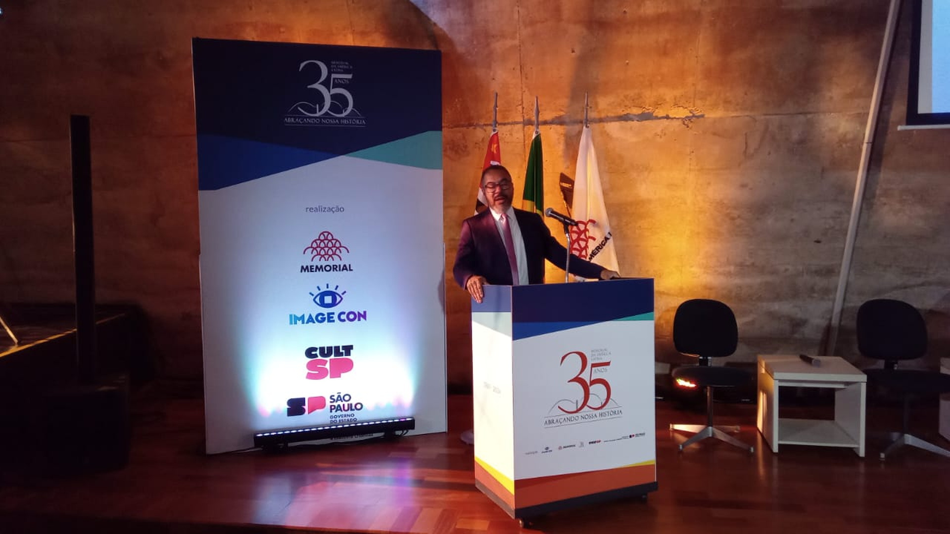 Una invitada habla en el atril ante un panel conmemorativo de los 35 años del Memorial da América Latina