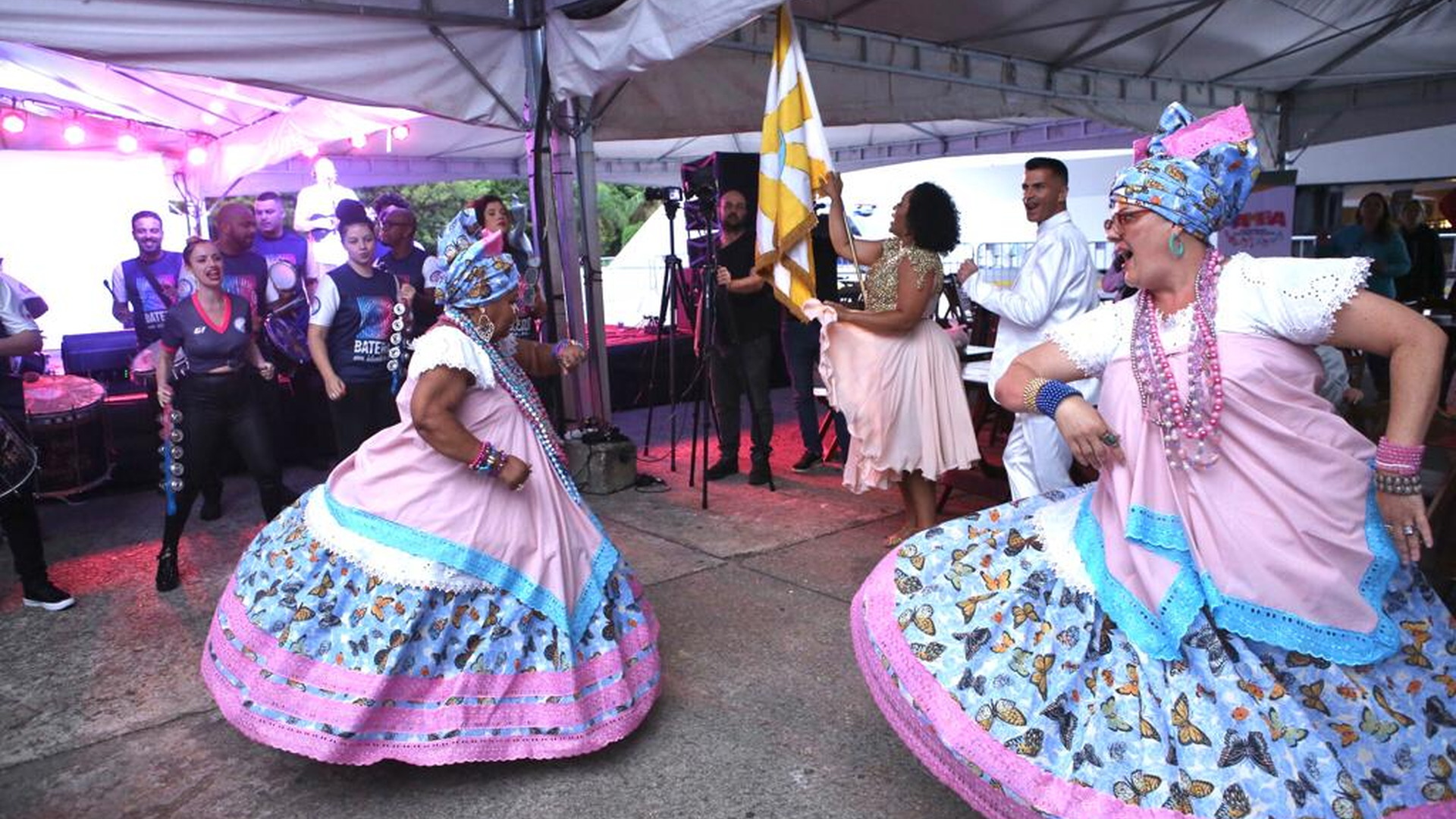 Dos artistas con trajes tradicionales bailan en un área exterior durante la programación cultural
