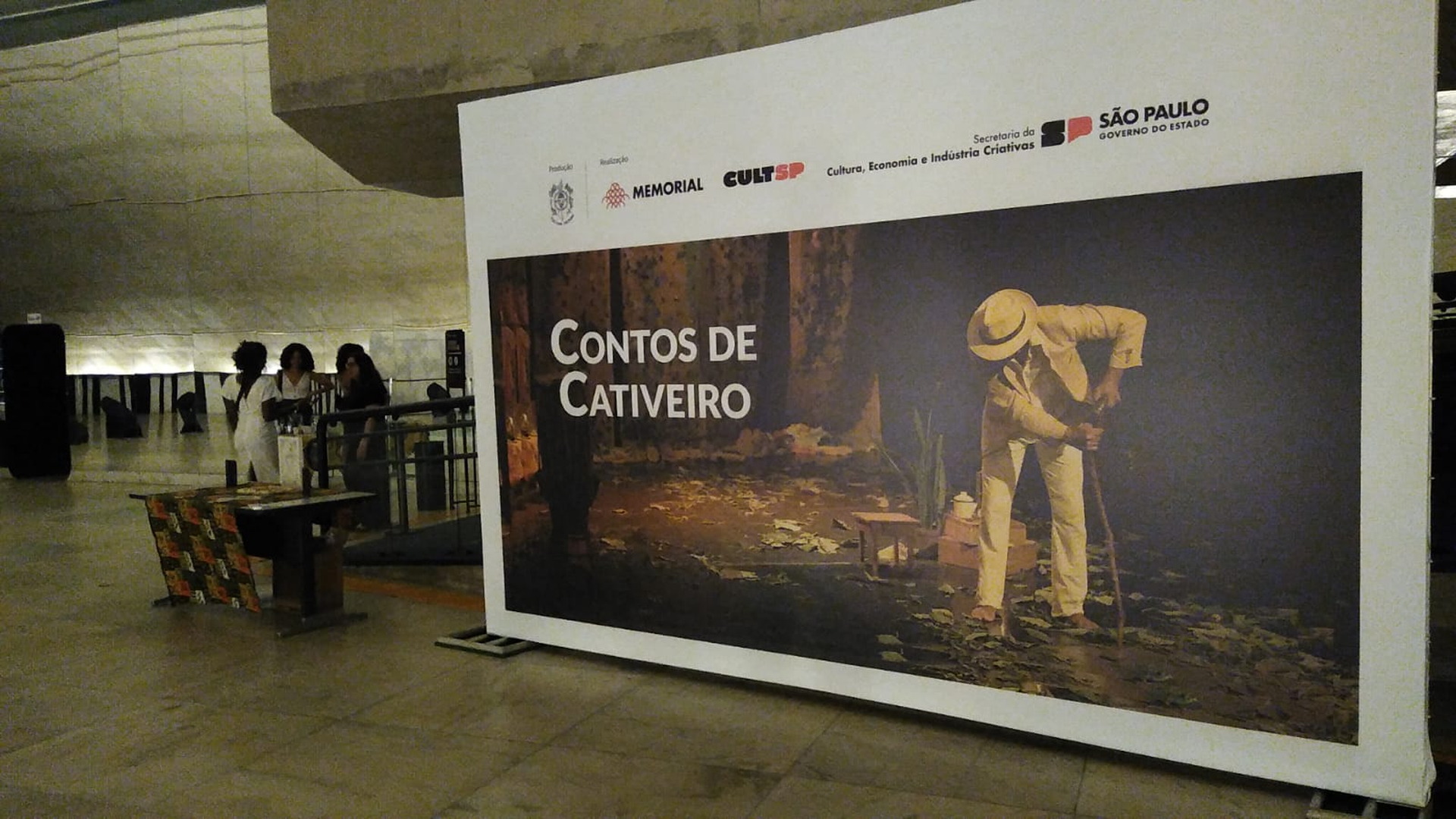Panel de difusión del espectáculo Contos de Cativeiro instalado en la entrada de un espacio de presentación