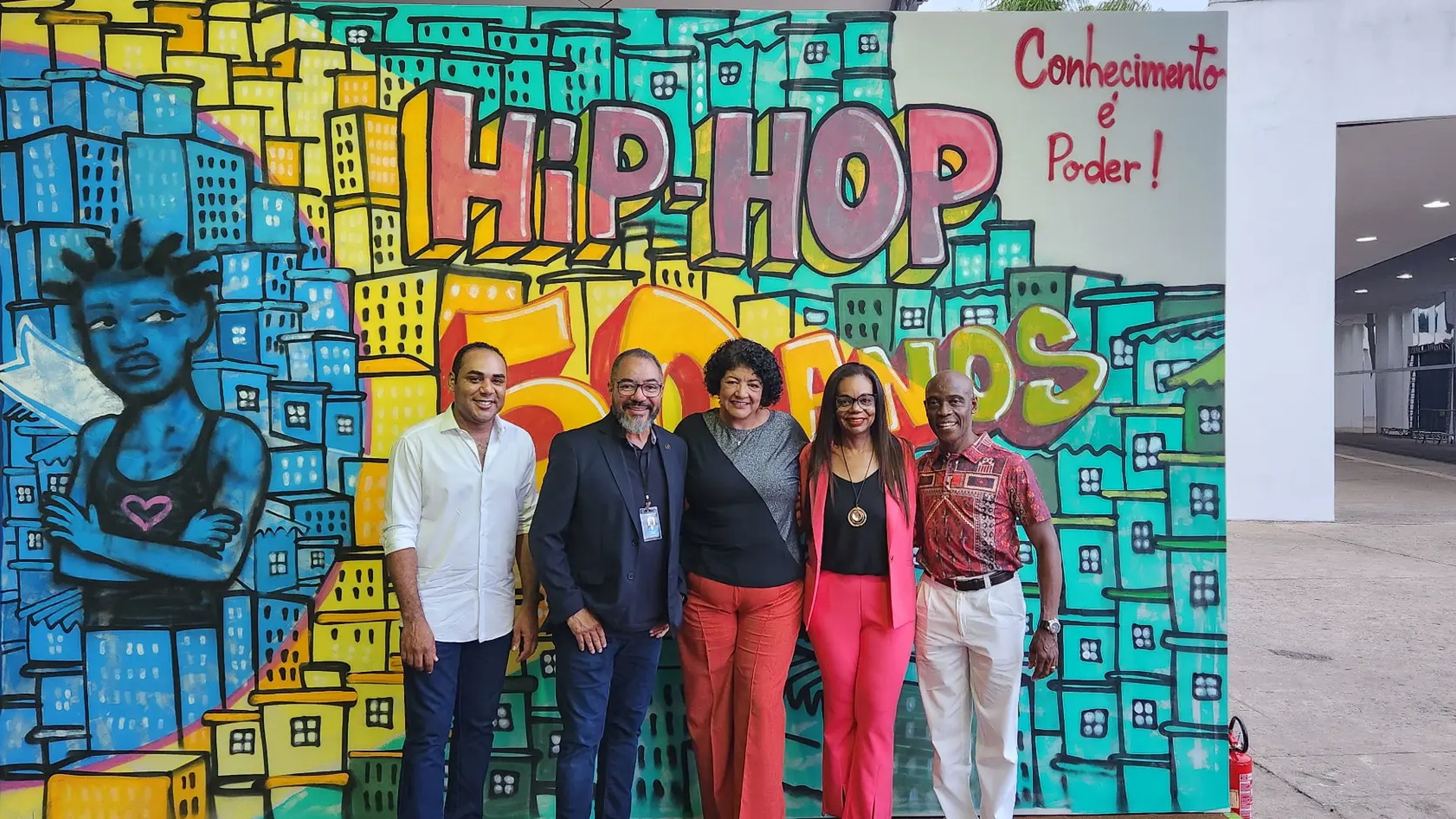João Carlos Corrêa e invitados posan ante un mural colorido sobre la historia del hip-hop