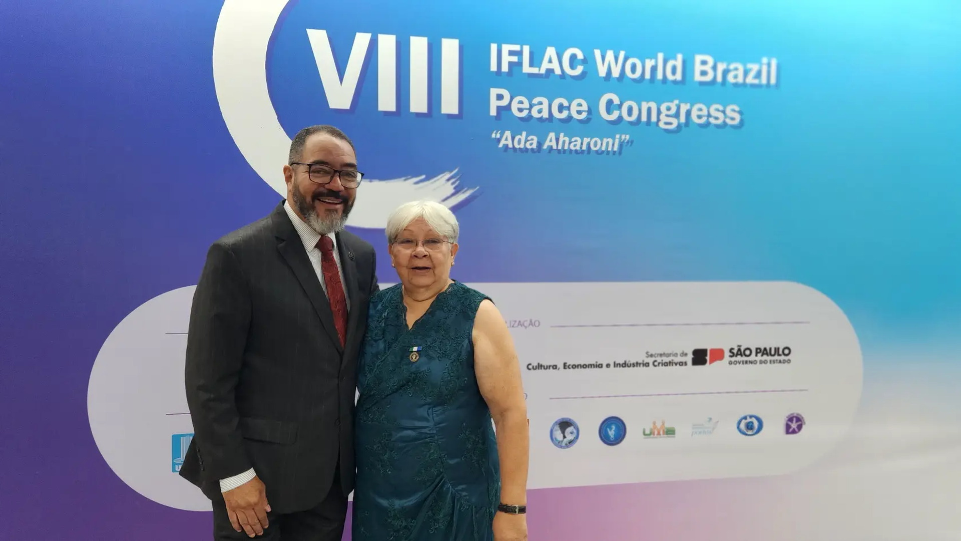 João Carlos Corrêa y un participante posan ante el panel del VIII IFLAC World Brazil Peace Congress