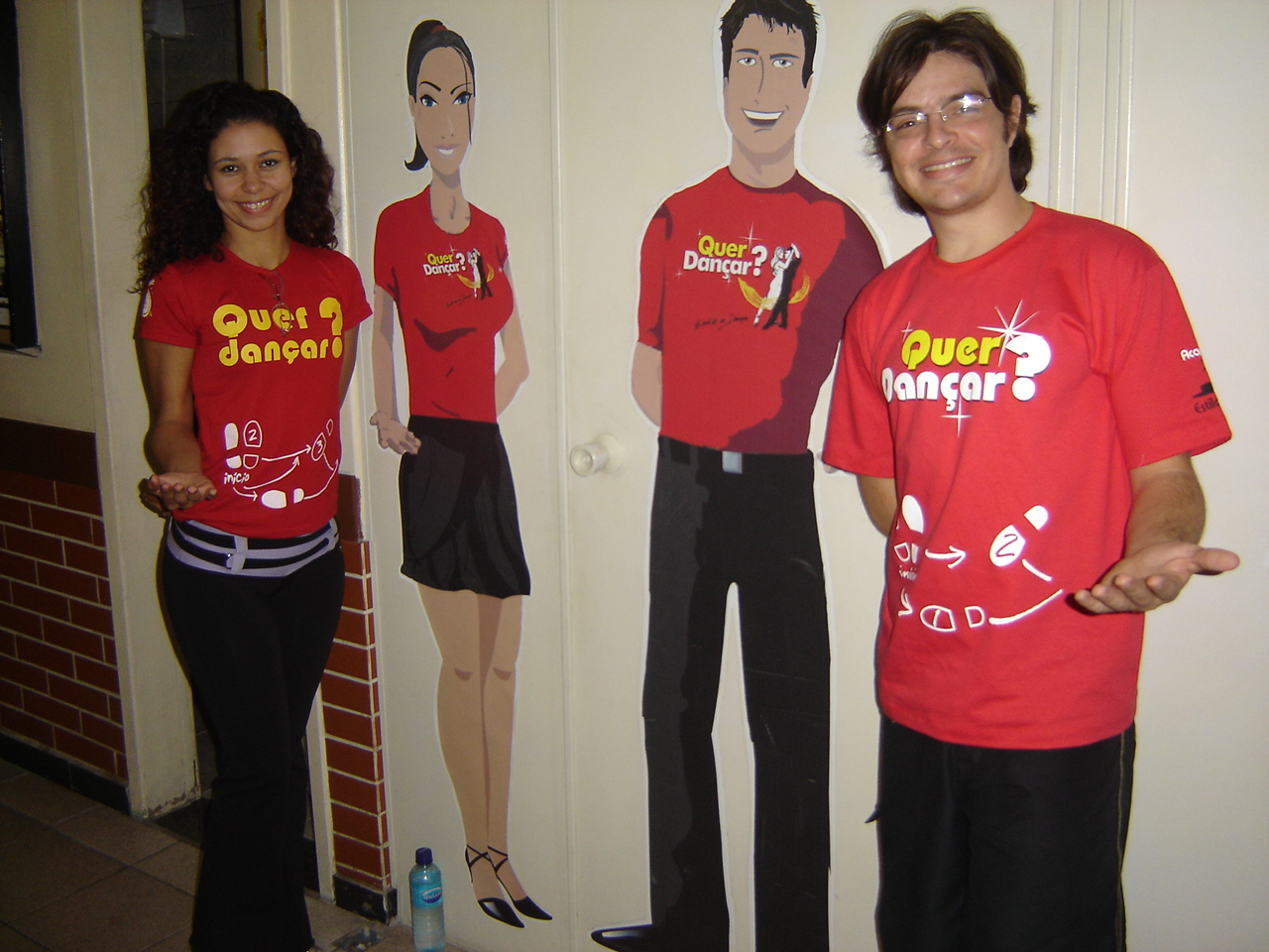 Dois integrantes com camisetas da Academia Estilo e Dança posam junto a figuras promocionais