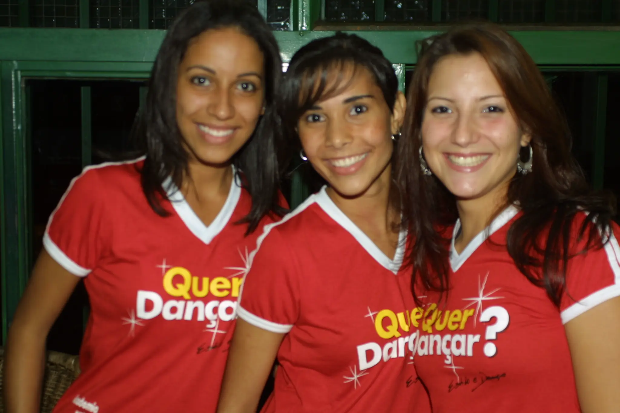 Três integrantes com camisetas vermelhas da campanha Quer Dançar reunidas em retrato