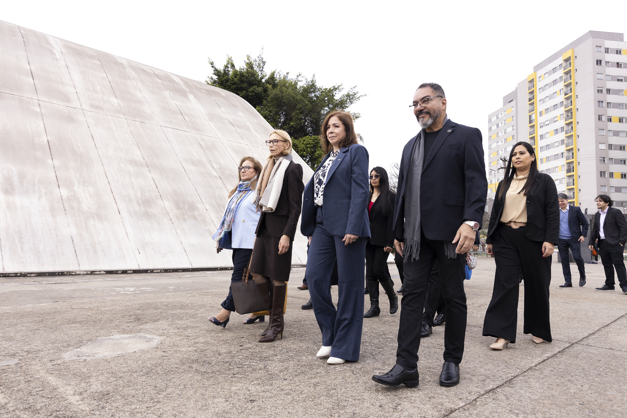 Grupo de participantes con vestimenta formal camina por el área exterior del Memorial da América Latina durante la agenda del Bicentenario