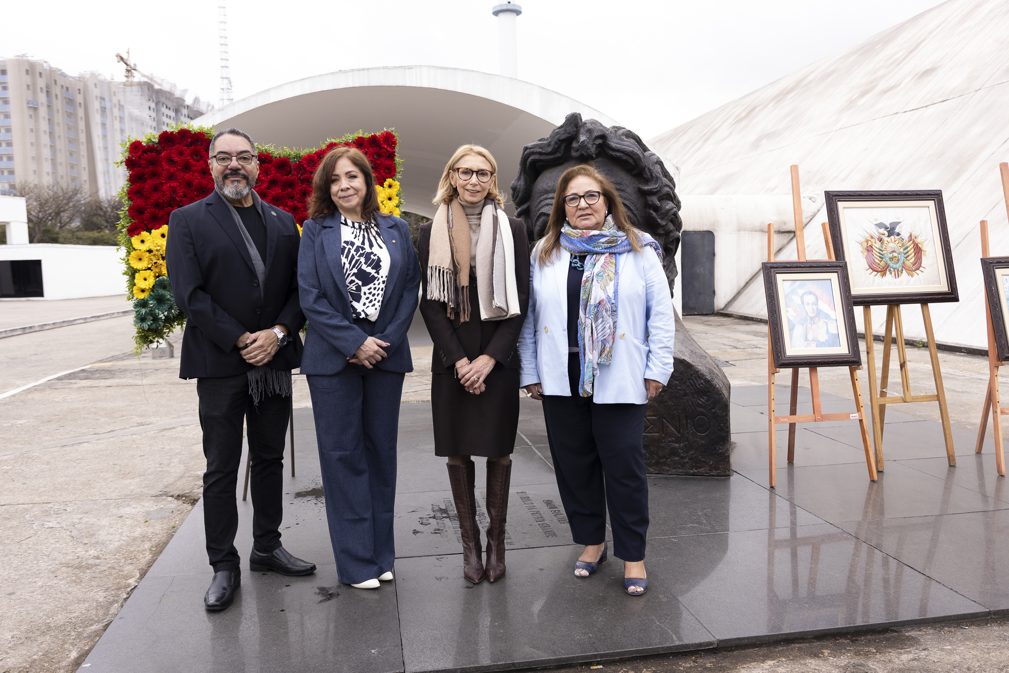 Cuatro participantes posan junto a un busto, un arreglo floral con los colores bolivianos y retratos expuestos en caballetes