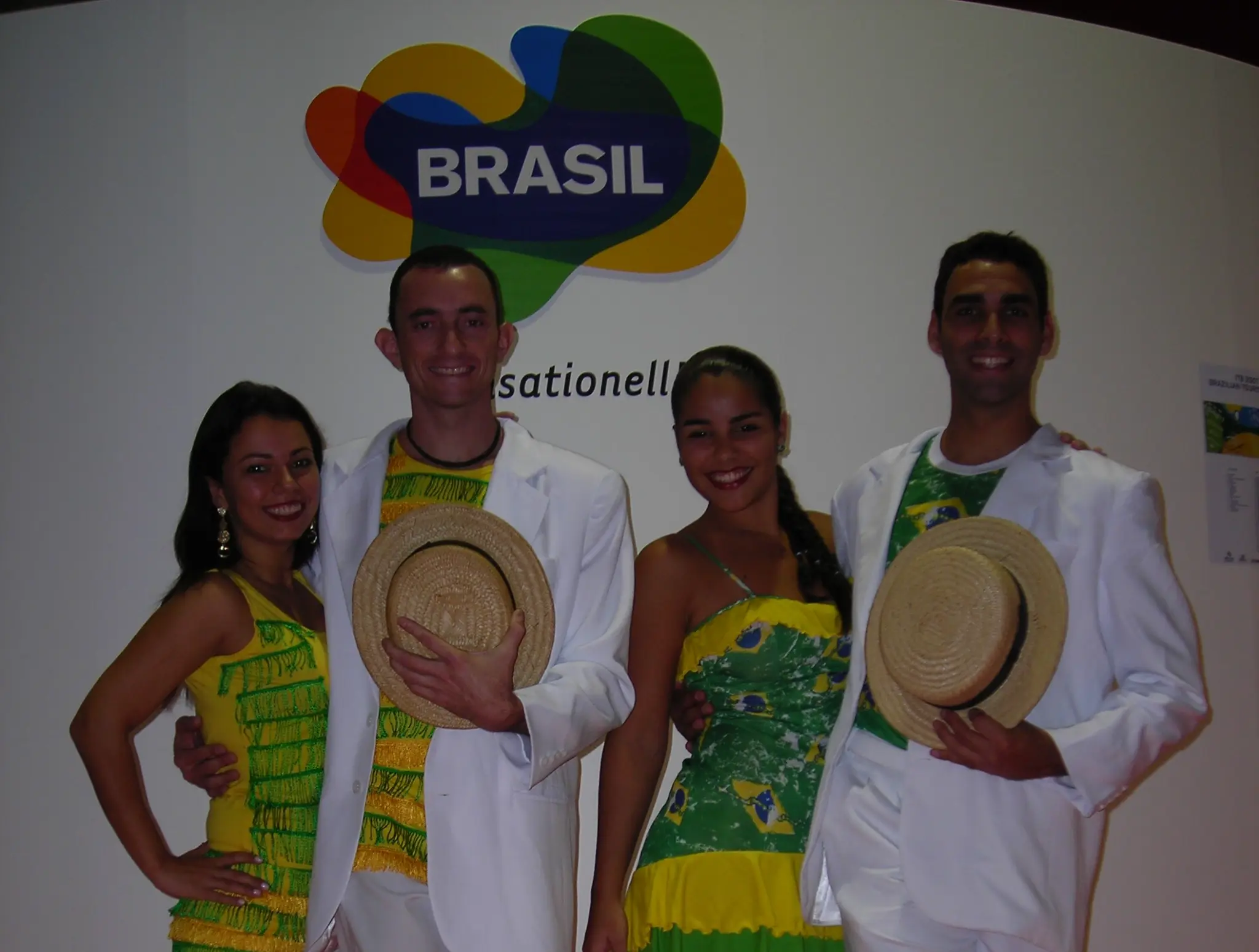 Quatro integrantes do Grupo Brasilidade reunidos com figurinos e chapéus diante da identidade visual do Brasil em Berlim, em 2007