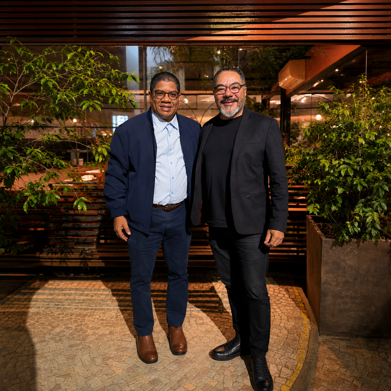 João Carlos Corrêa posa junto a un representante cubano en un ambiente exterior con plantas y estructura de madera