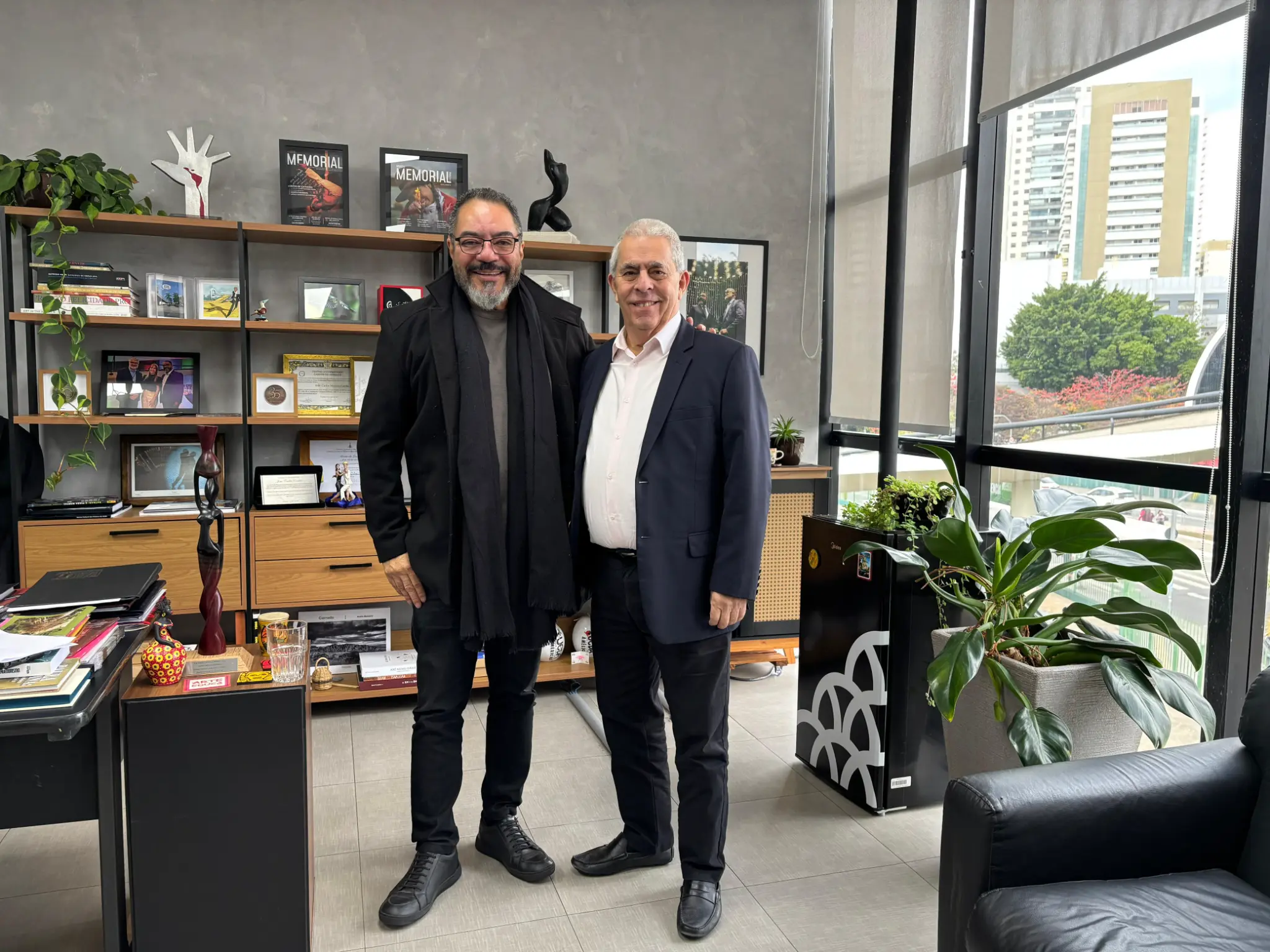 João Carlos Corrêa posa junto a un representante en una oficina del Memorial, con estantería, publicaciones y vista al conjunto arquitectónico