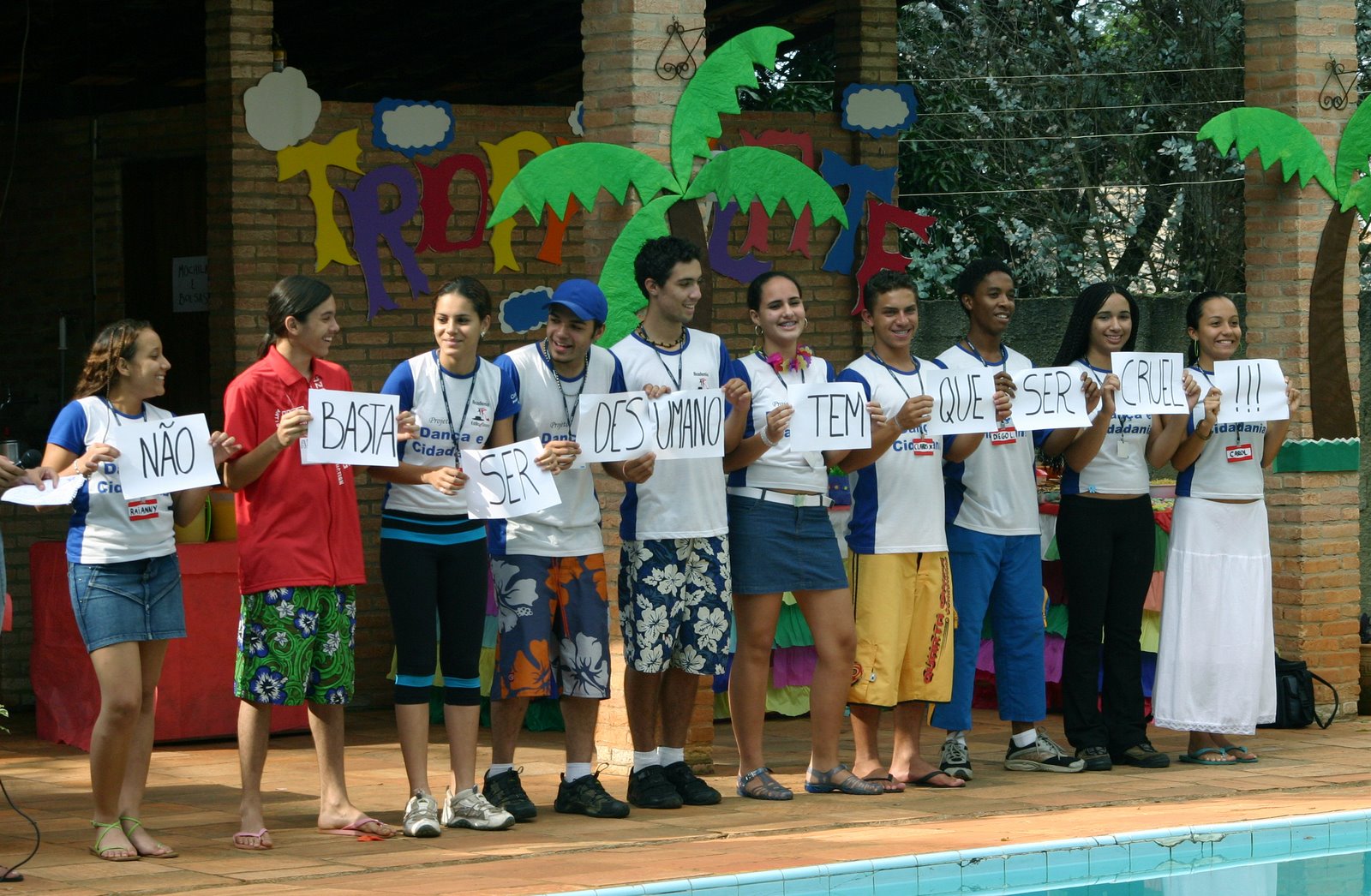 Participantes do Projeto Dança e Cidadania formam uma fila e exibem placas escritas durante uma ação cênica