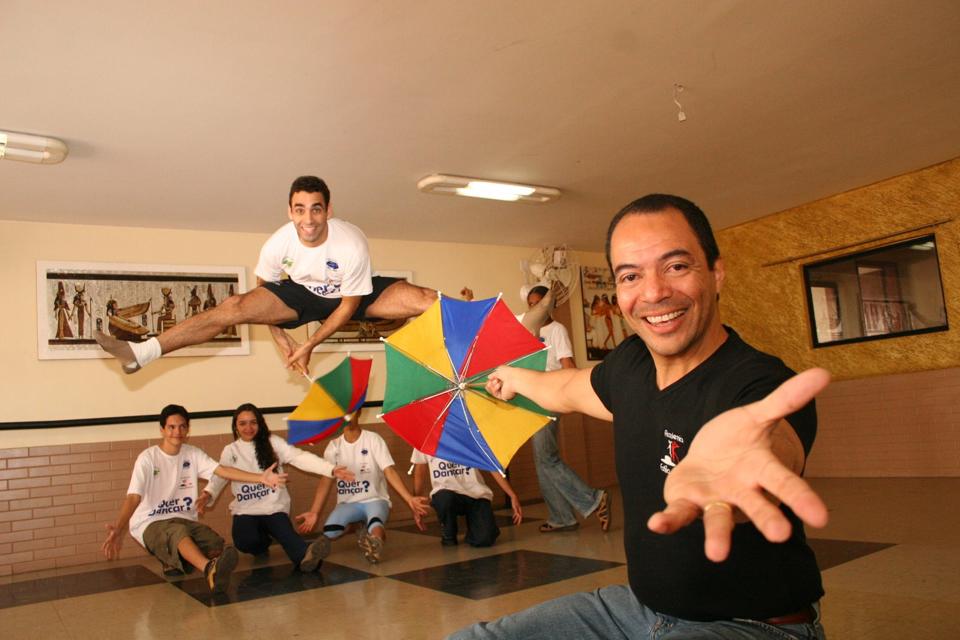 João Carlos Corrêa e participantes realizam ação cênica com guarda-chuvas coloridos em ambiente interno