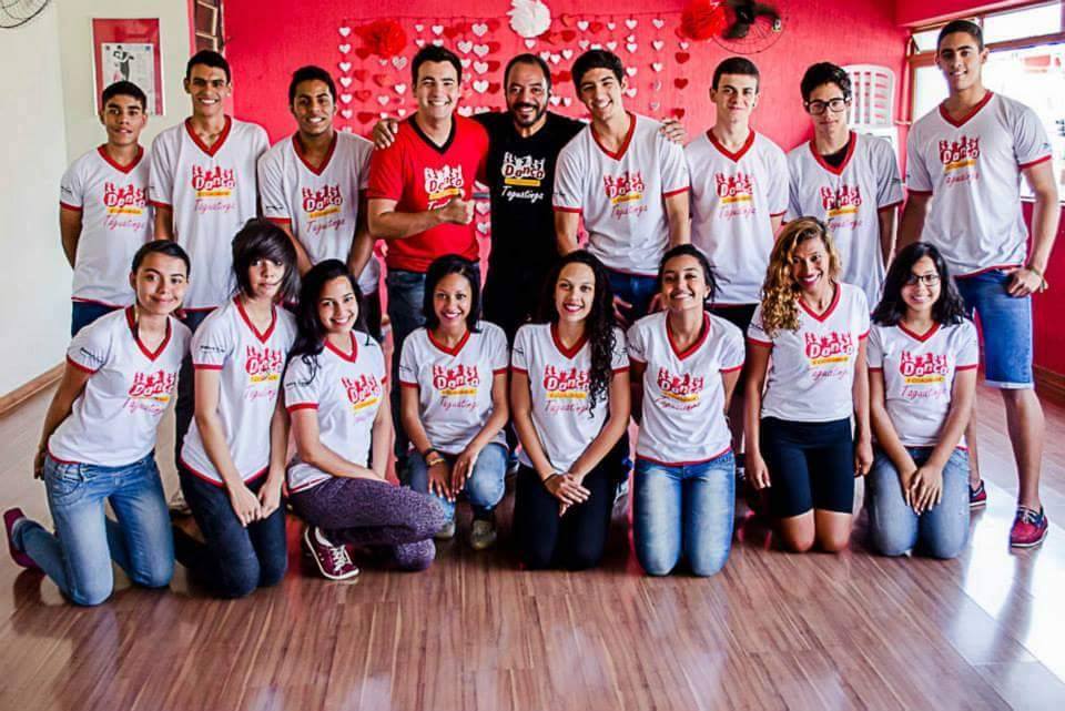 Casais praticam dança em formação coletiva dentro de uma sala de aula
