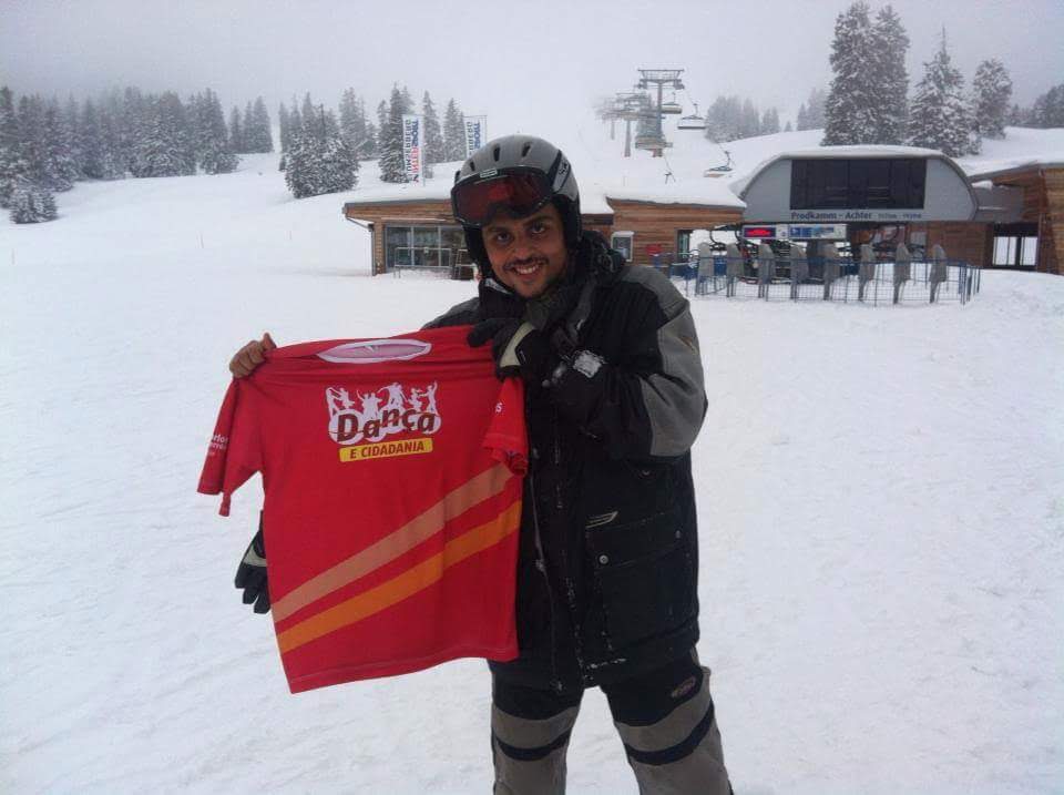 Pessoa em ambiente de neve segura uma camiseta vermelha com a identidade do Projeto Dança e Cidadania