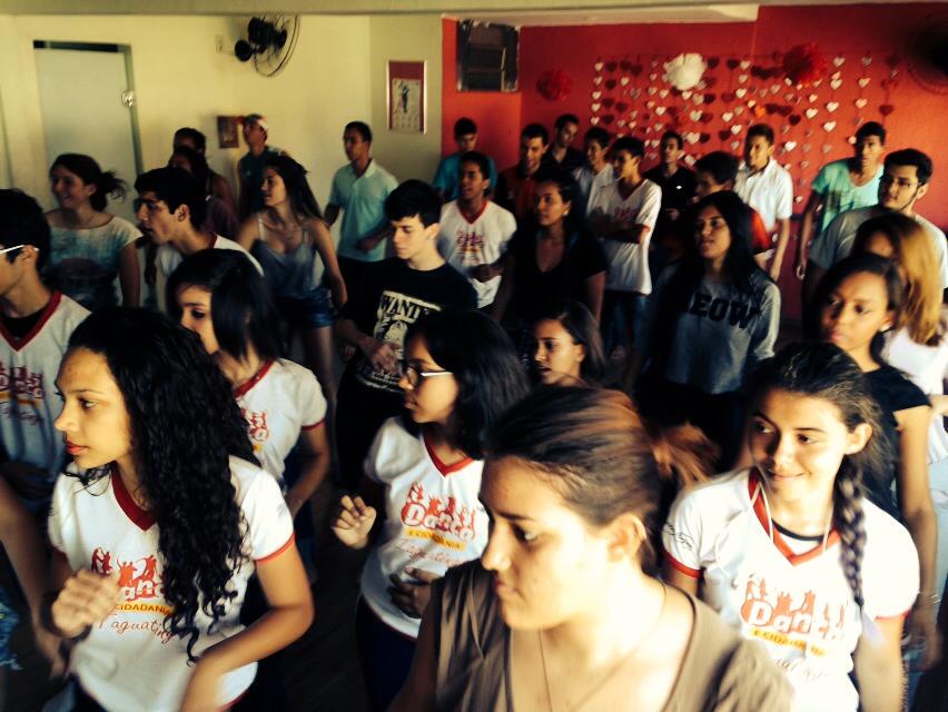 Jovem orienta uma participante durante prática de dança em sala de aula