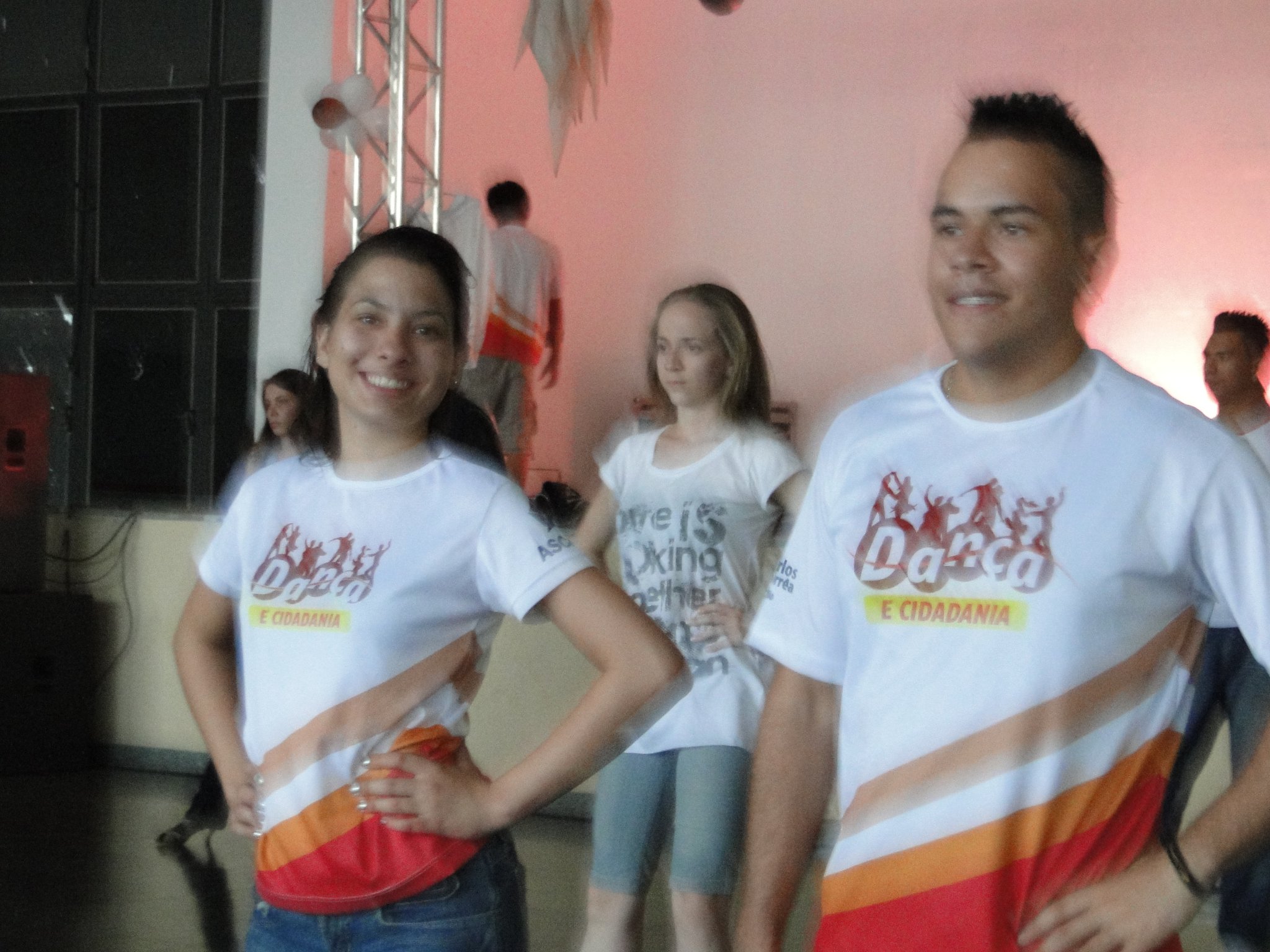 Dois participantes com camisetas do Projeto Dança e Cidadania em primeiro plano durante atividade coletiva