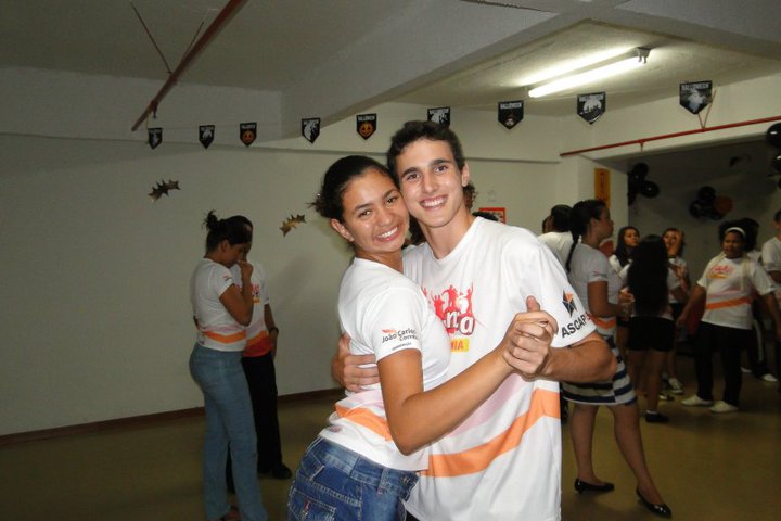 Dois jovens participantes praticam dança de salão em um espaço de aula, usando camisetas da ASCAPIS