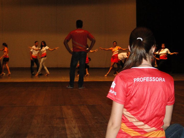 Participantes com figurinos coloridos formam uma roda durante apresentação coletiva