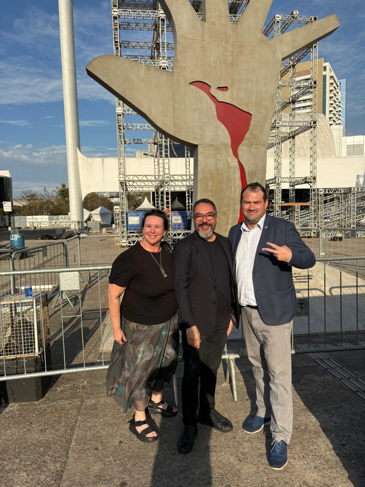 Dina E. Thrasher, João Carlos Corrêa y Gavin Nardocchio-Jones posan frente a la escultura A Mão en la Praça Cívica del Memorial