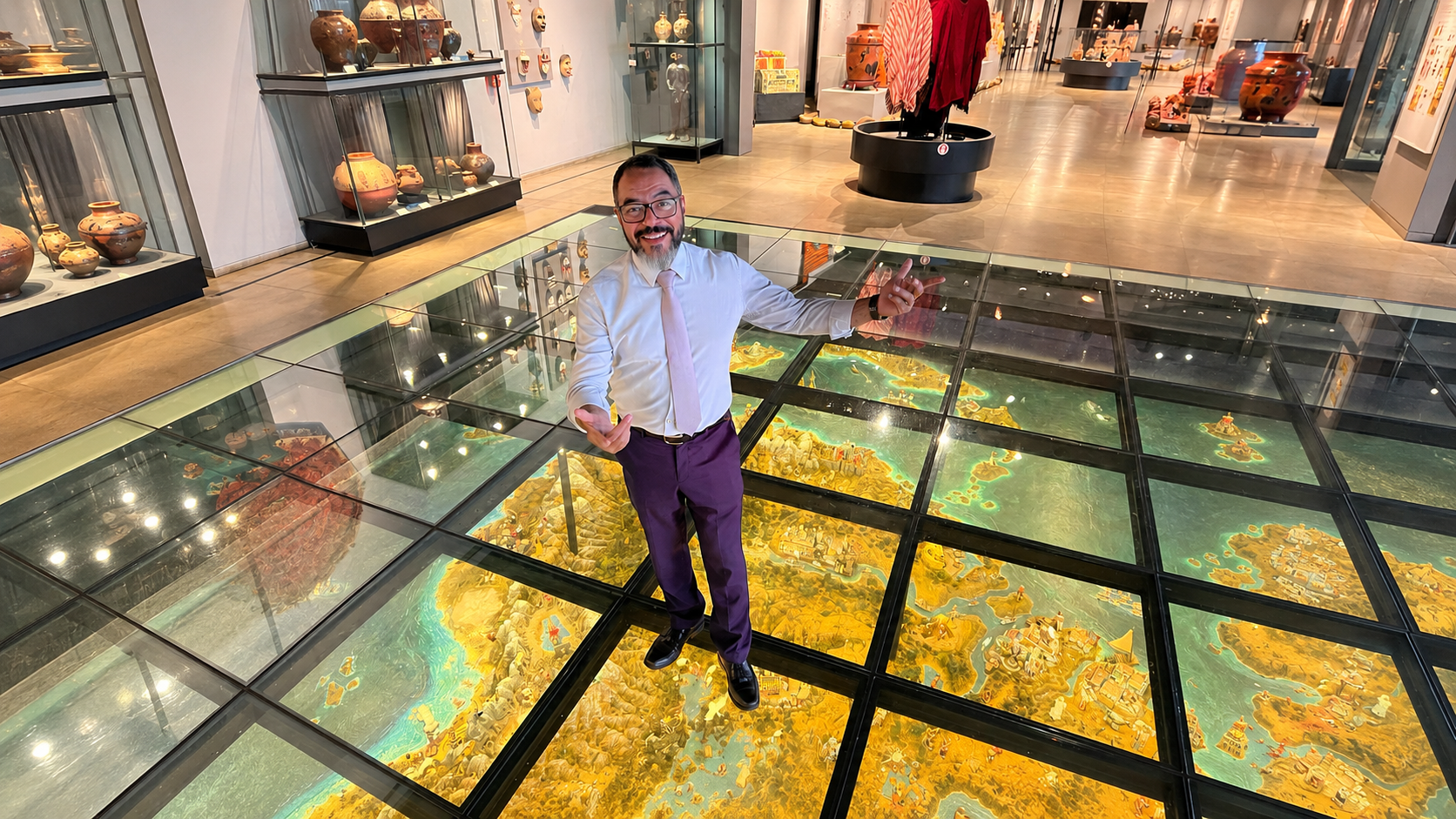 João Carlos Corrêa em uma galeria museológica, sobre piso de vidro com maquete cartográfica iluminada e acervos expostos ao redor
