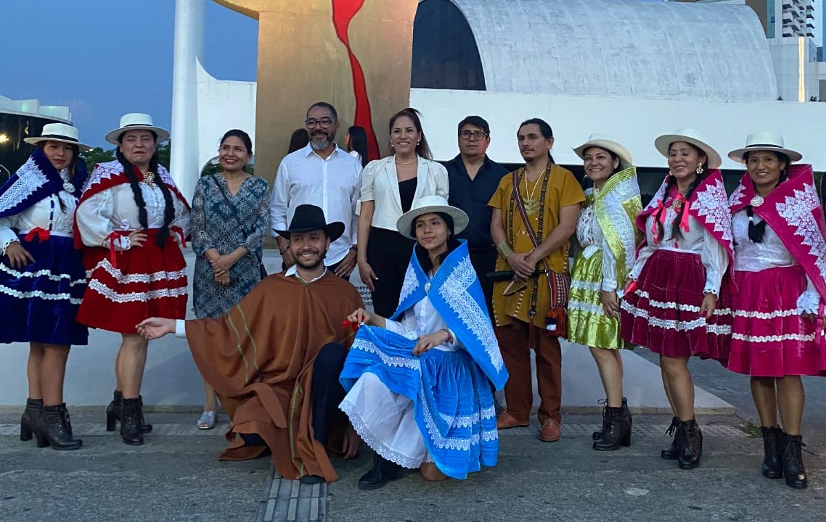 João Carlos Corrêa posa con un grupo de participantes, varios de ellos con coloridos trajes tradicionales peruanos, frente al monumento A Mão
