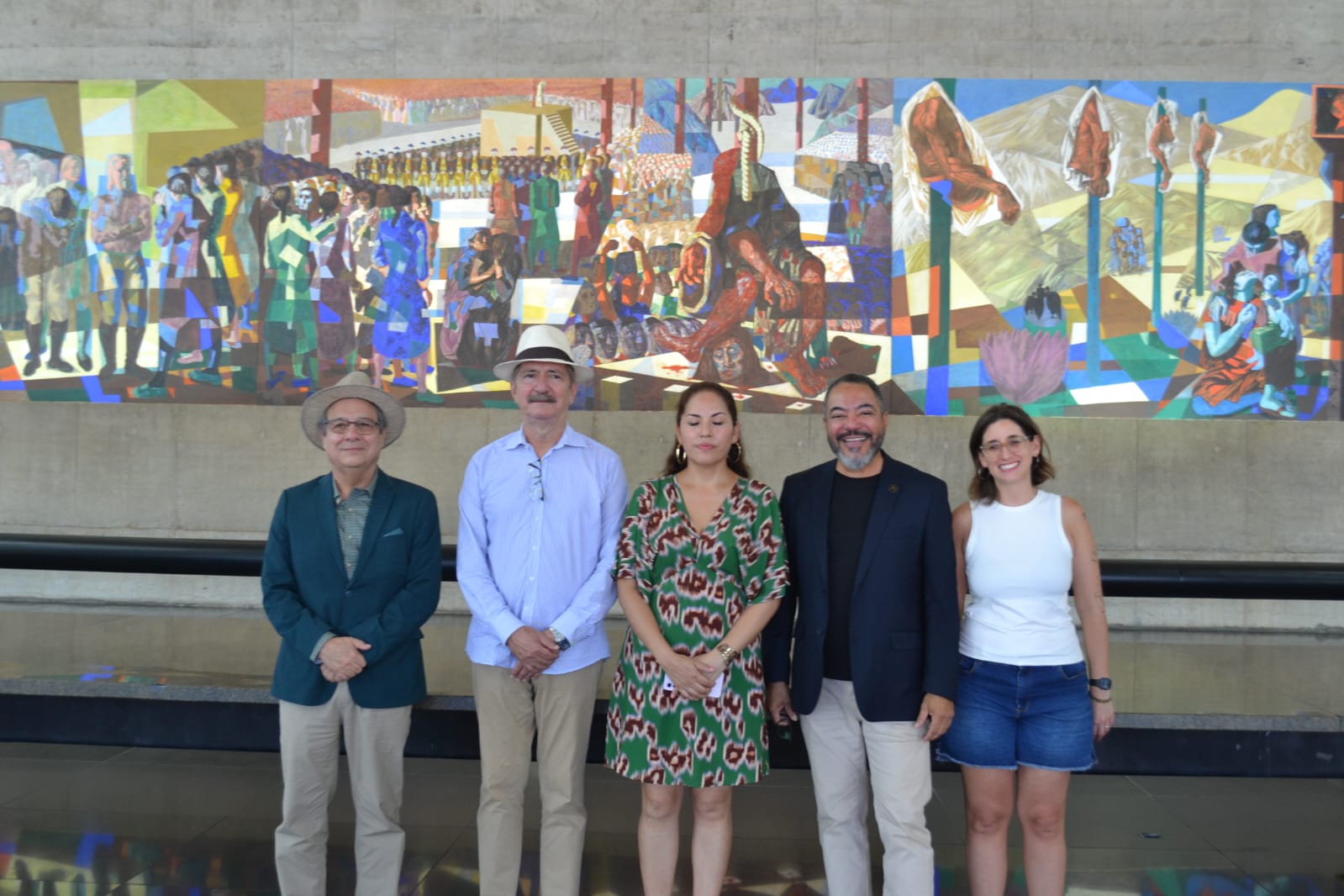 João Carlos Corrêa y cuatro visitantes posan frente a un gran mural colorido en el interior del Memorial da América Latina