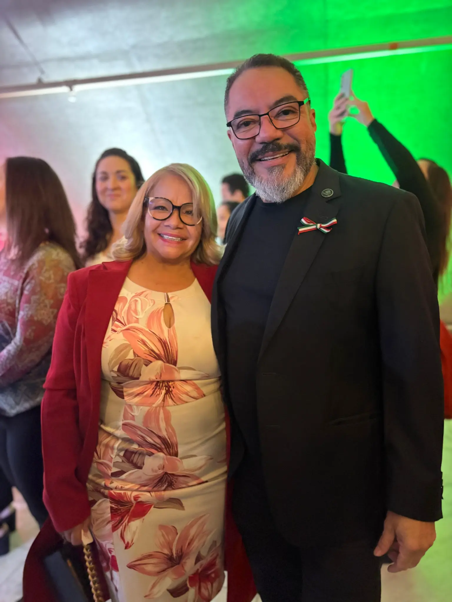 Hanoi Sánchez Paniagua y João Carlos Corrêa sonríen lado a lado entre participantes de un evento con iluminación verde al fondo