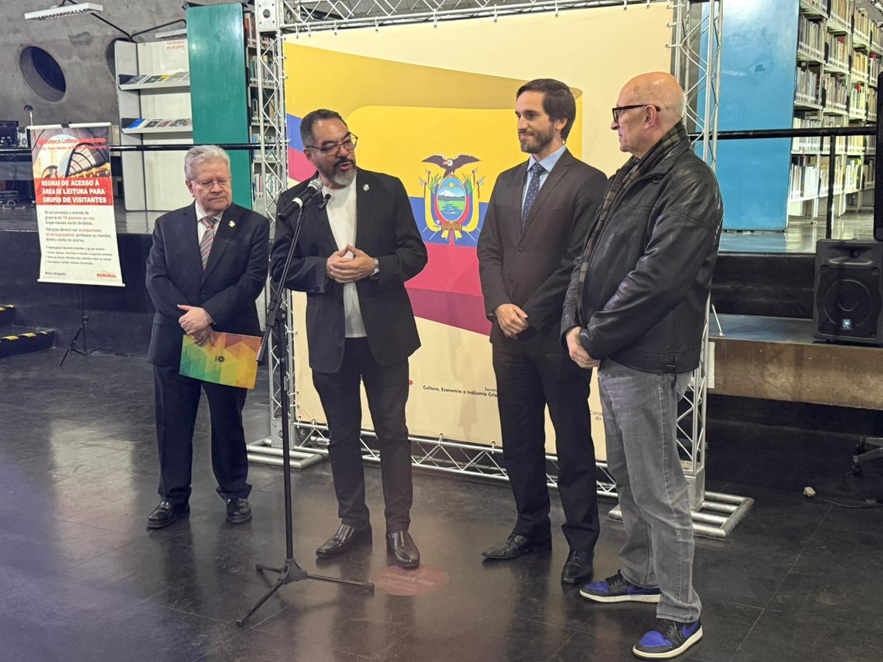 João Carlos Corrêa e invitados participan en la inauguración de la exposición ante la bandera de Ecuador y un panel artístico