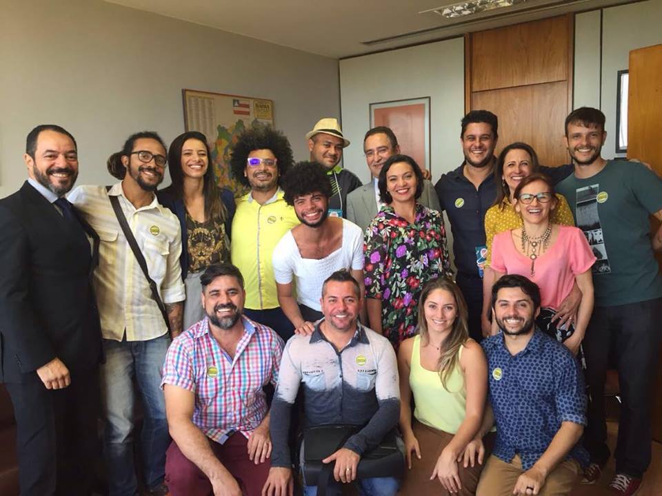 Grupo numeroso de participantes da articulação pela dança posa reunido em ambiente de gabinete.
