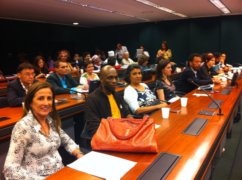 Participantes ocupam bancadas com microfones e acompanham uma reunião de trabalho em ambiente legislativo.