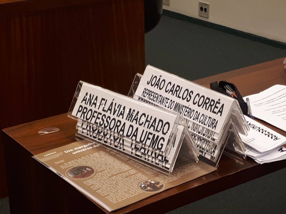 Uma participante fala ao microfone em palco durante atividade cultural e institucional.