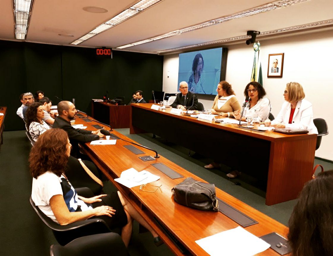 Uma participante fala ao microfone em mesa de debate diante do público.