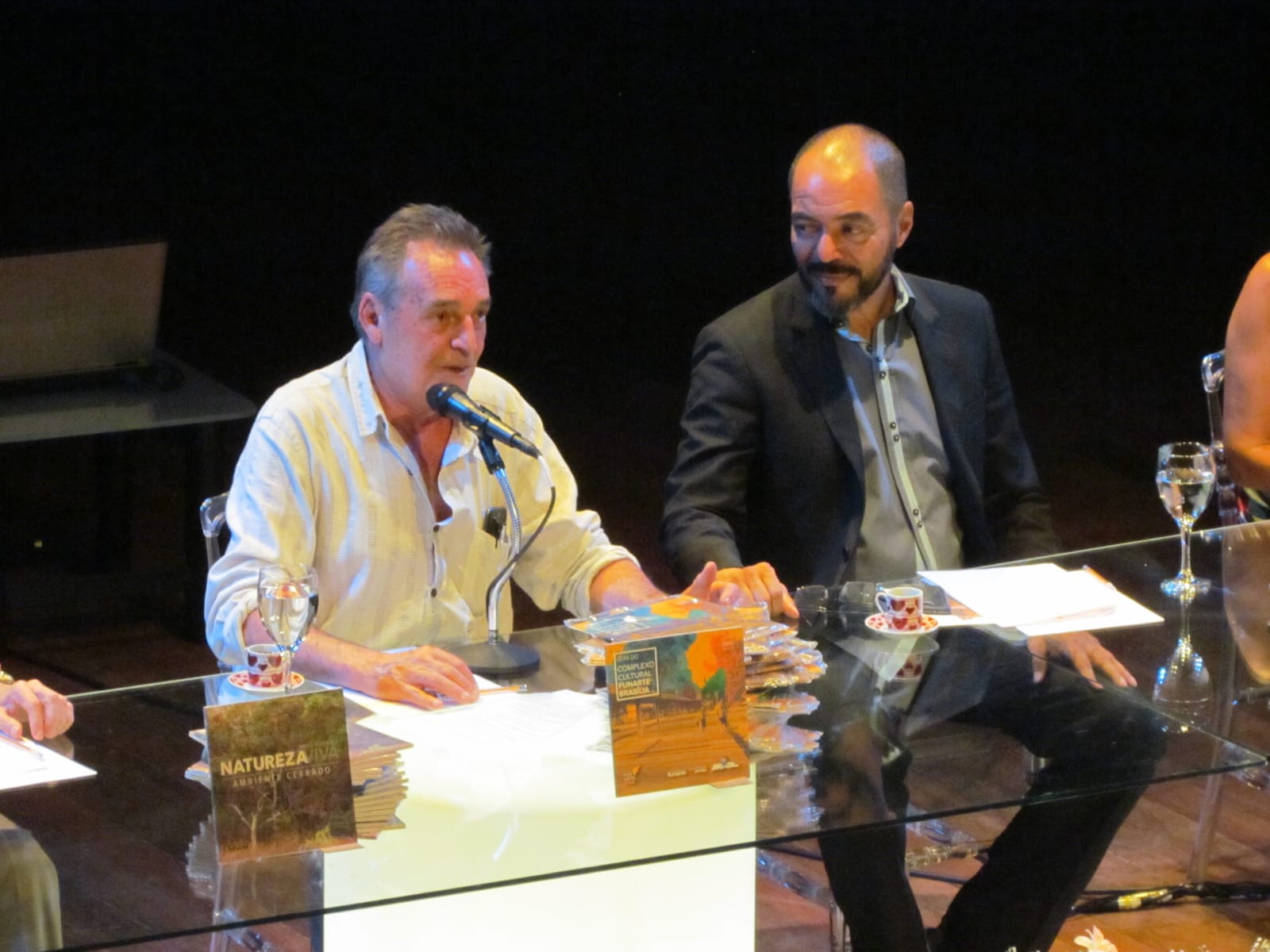 Participantes em mesa de lançamento de publicações na Funarte Brasília, com livros expostos e um convidado falando ao microfone