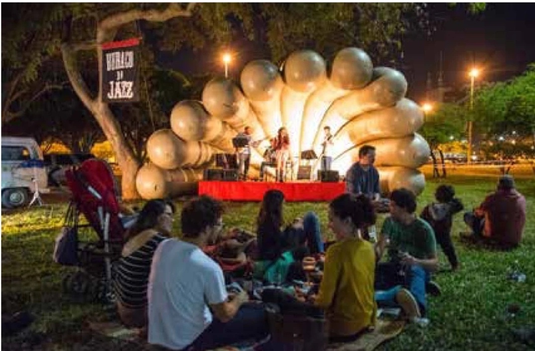 Público sentado no gramado diante do palco iluminado do Buraco do Jazz na área externa da Funarte Brasília