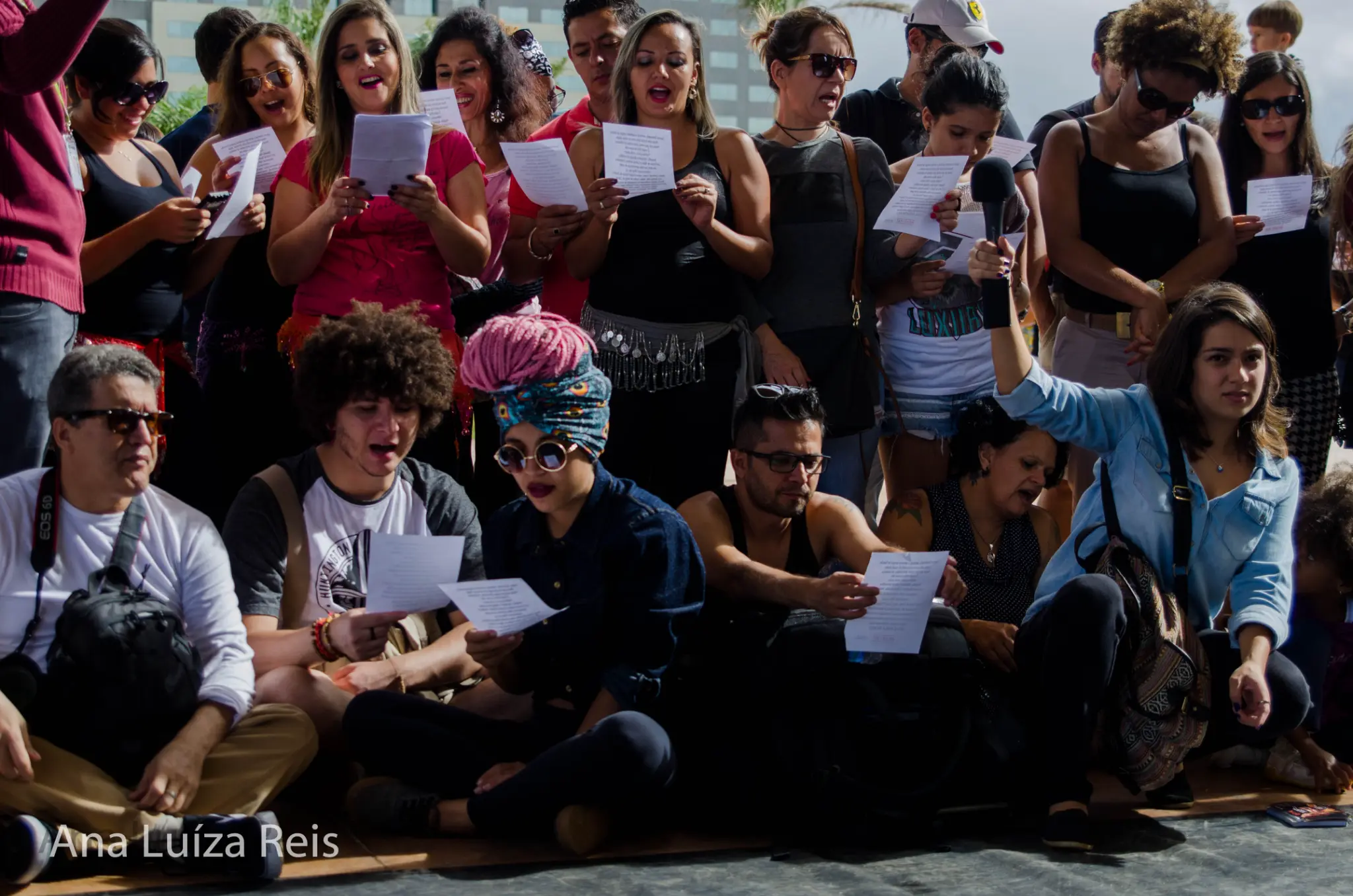 Grupo de participantes reunidos ao ar livre, parte deles com folhas impressas nas mãos.