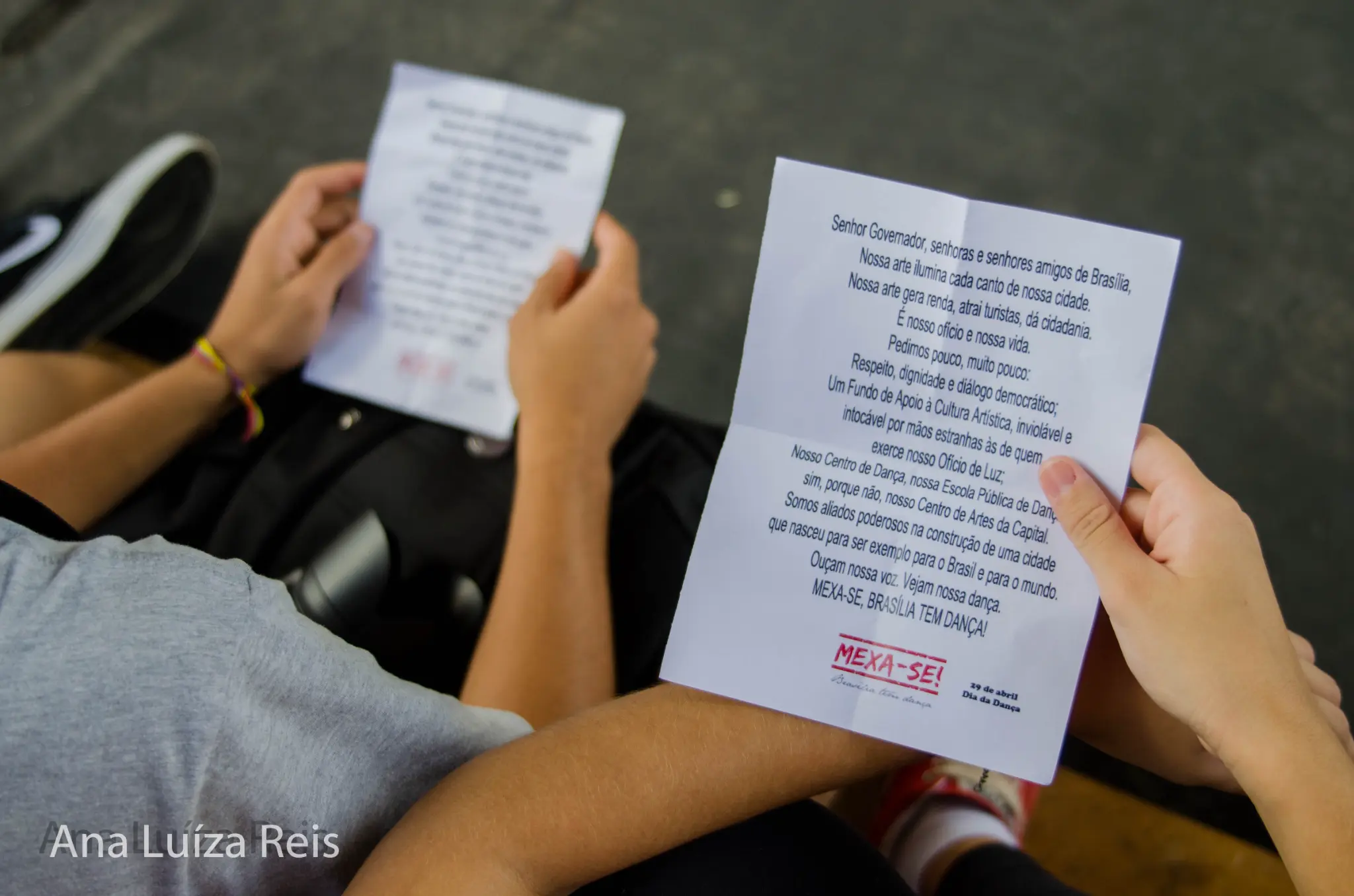 Detalhe de mãos segurando folhas impressas com o manifesto cultural do Grito da Dança.