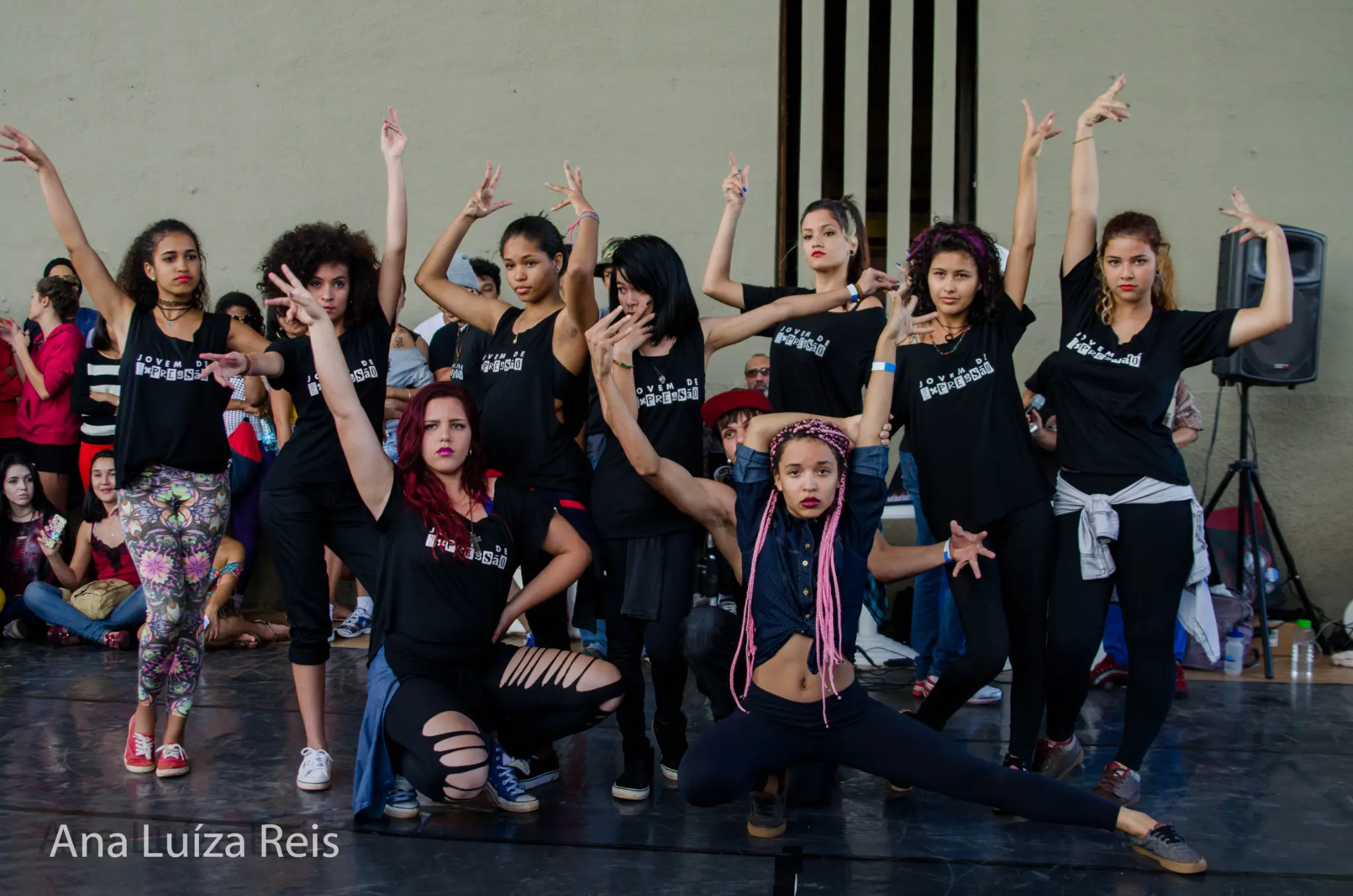 Grupo jovem com roupas escuras realiza uma composição coreográfica diante da plateia.