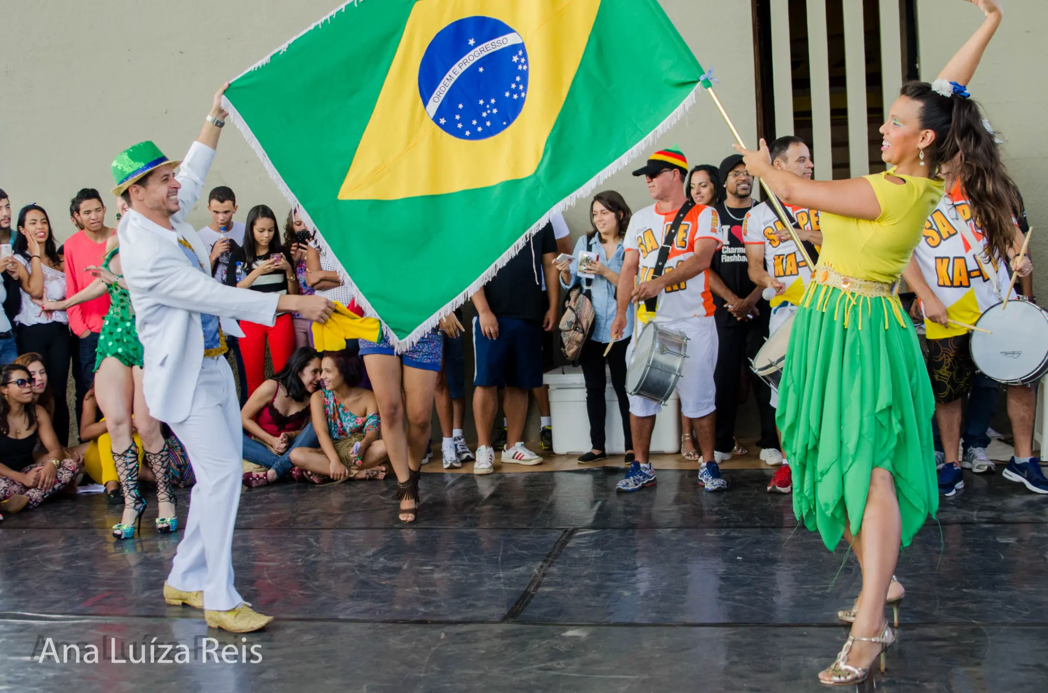 Dupla dança com a bandeira do Brasil diante de músicos e espectadores.