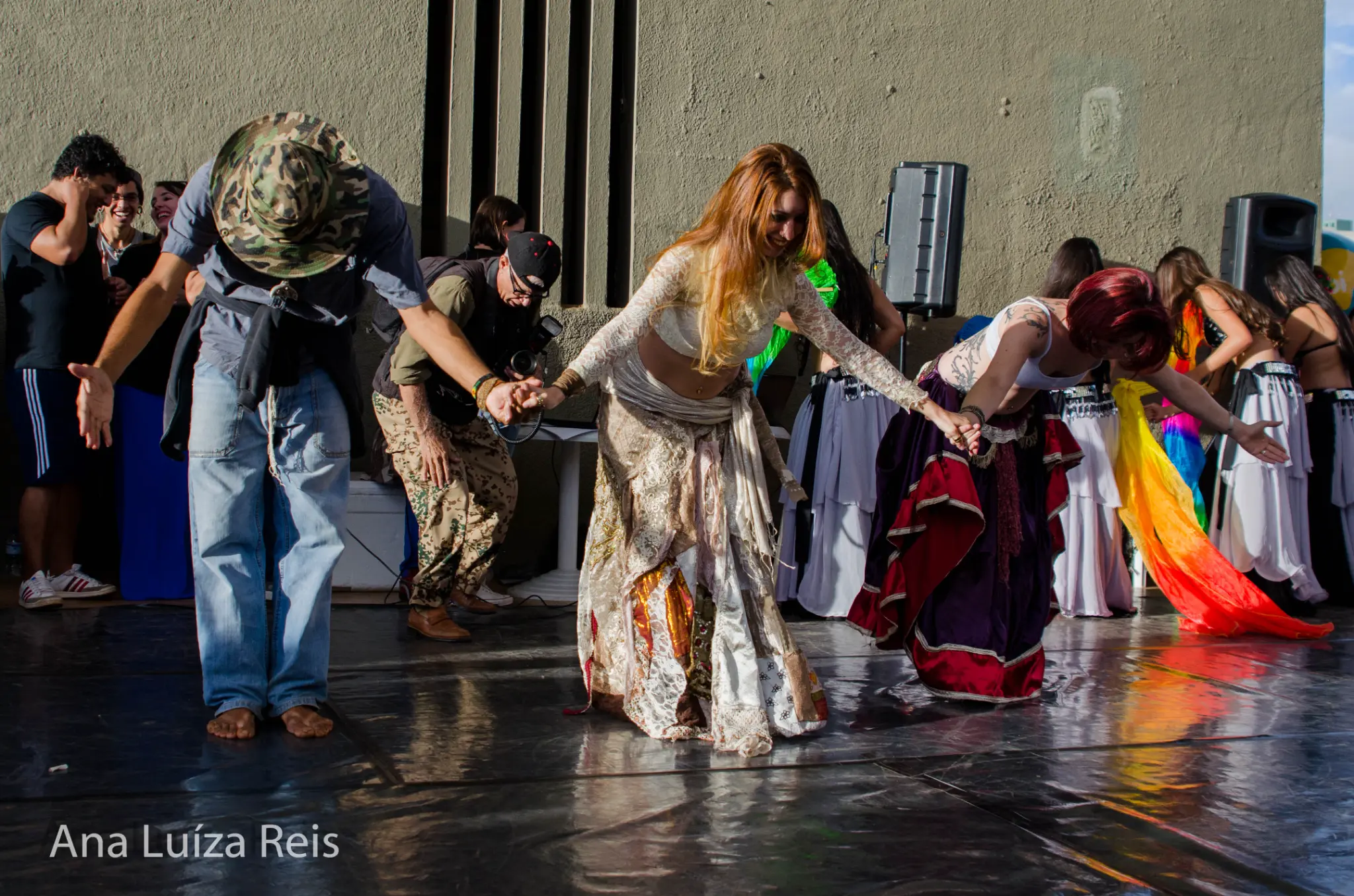 Grupo de participantes de mãos dadas se curva em gesto de agradecimento sobre o piso de dança.