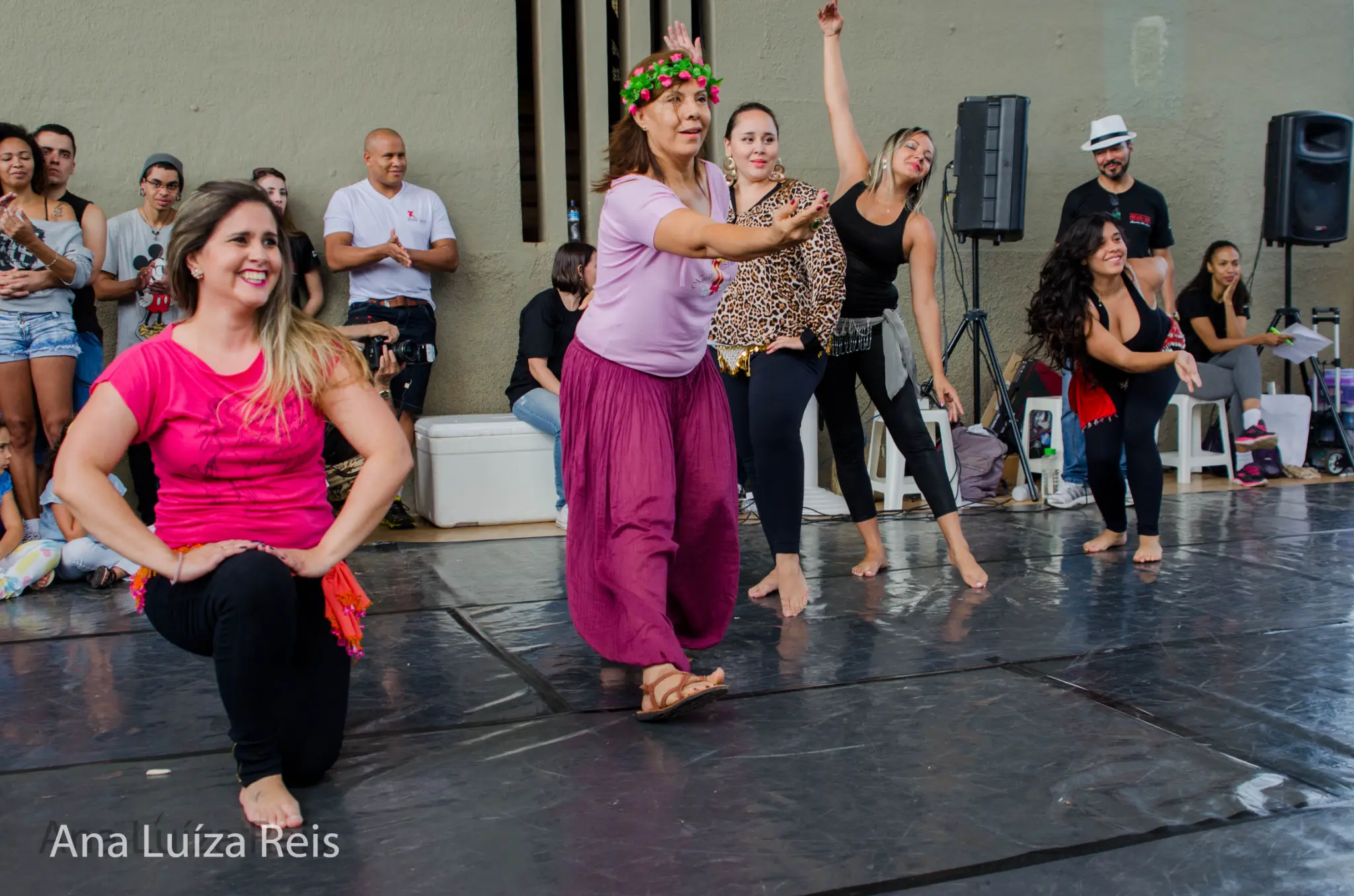 Grupo de mulheres realiza movimentos sincronizados sobre o piso de dança diante do público.