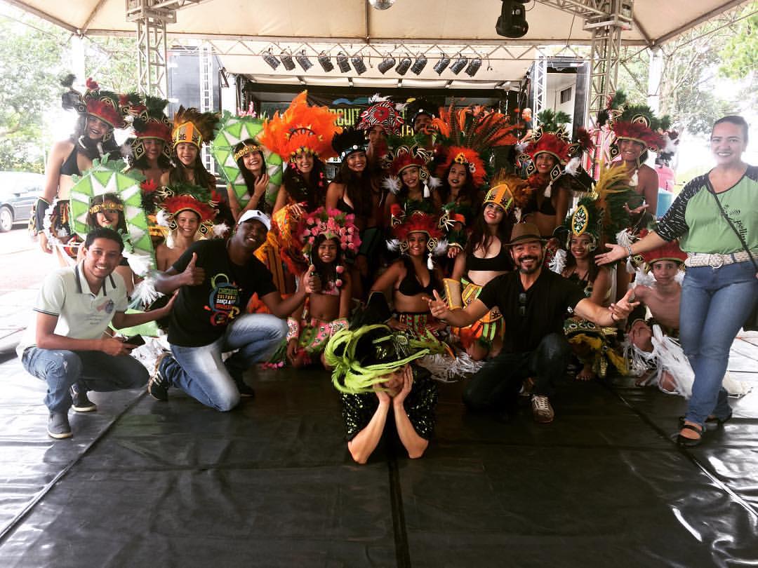 Grupo numeroso de artistas e equipe reunido no palco com figurinos coloridos durante o Circuito