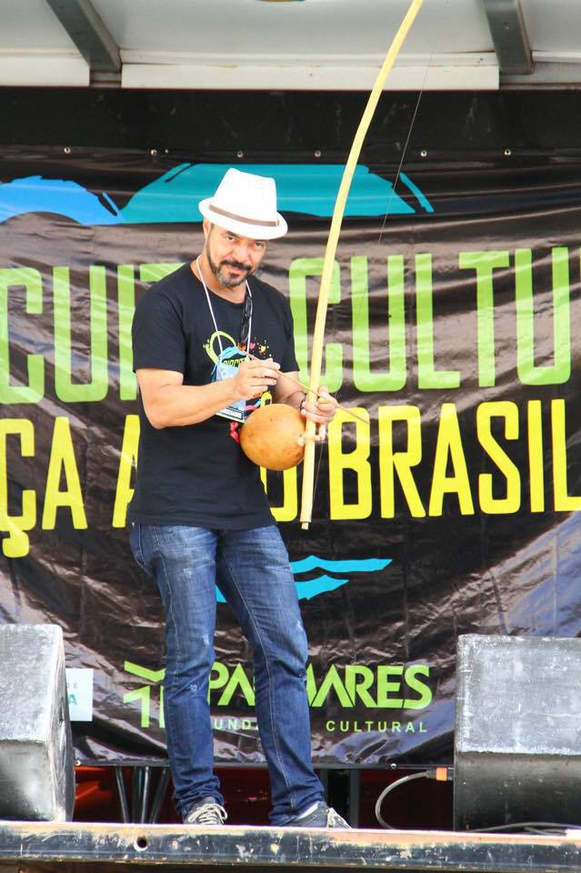 João Carlos Corrêa segura um berimbau diante do painel do Circuito Cultural de Danças Afro-Brasileiras
