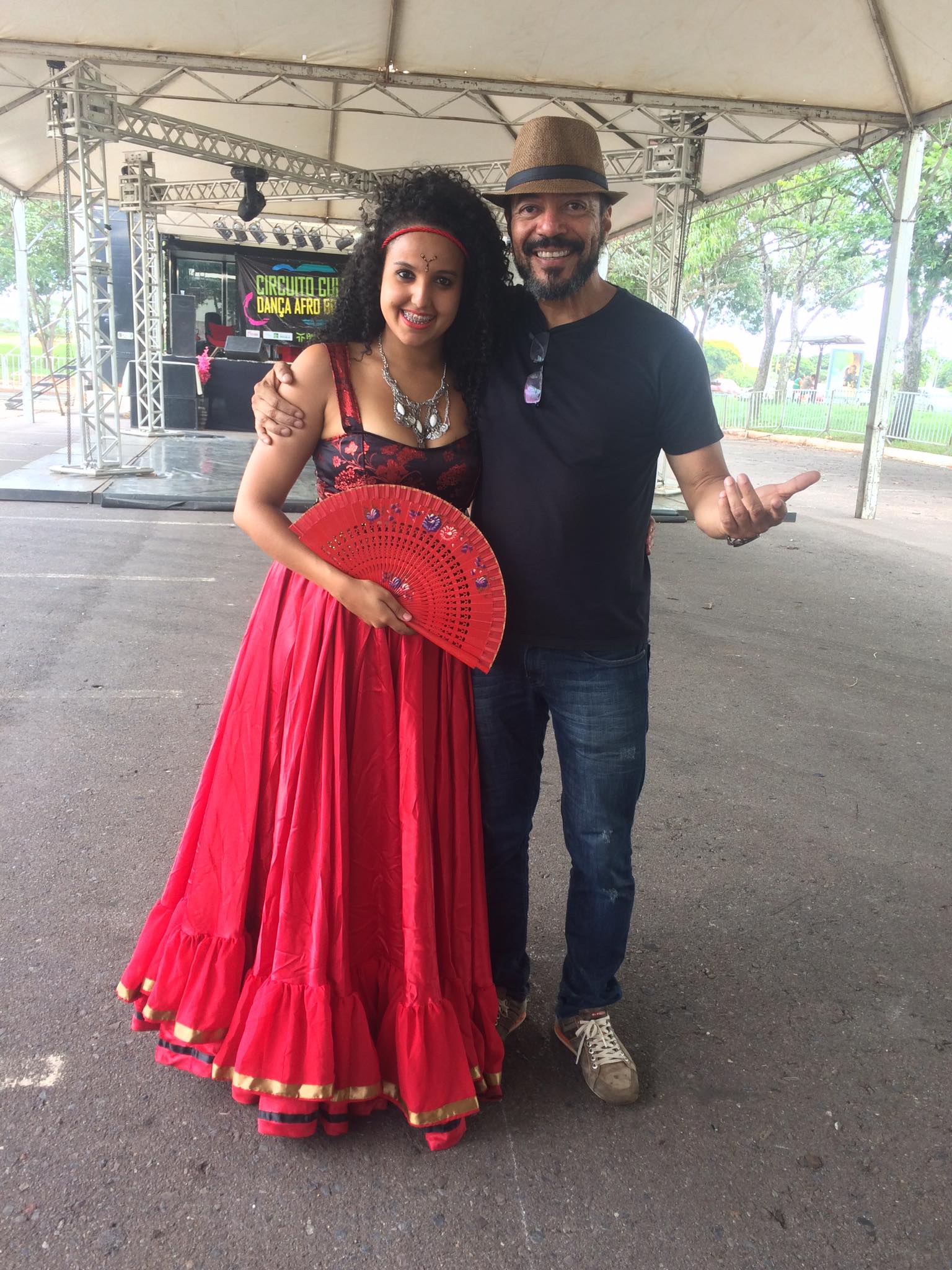 João Carlos Corrêa ao lado de uma artista com vestido vermelho e leque, diante do palco do Circuito