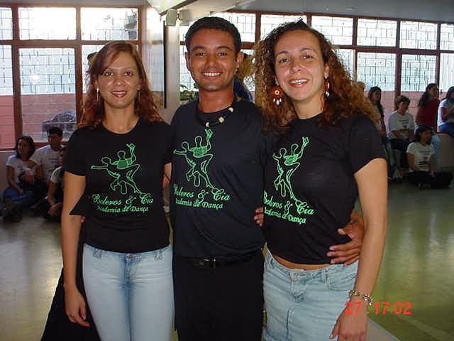Três integrantes com camisetas escuras da I Maratona de Dança reunidos no salão