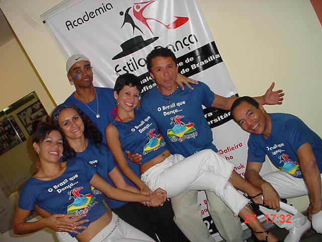 Grupo de integrantes uniformizados reunido diante da identidade visual da Academia Estilo e Dança