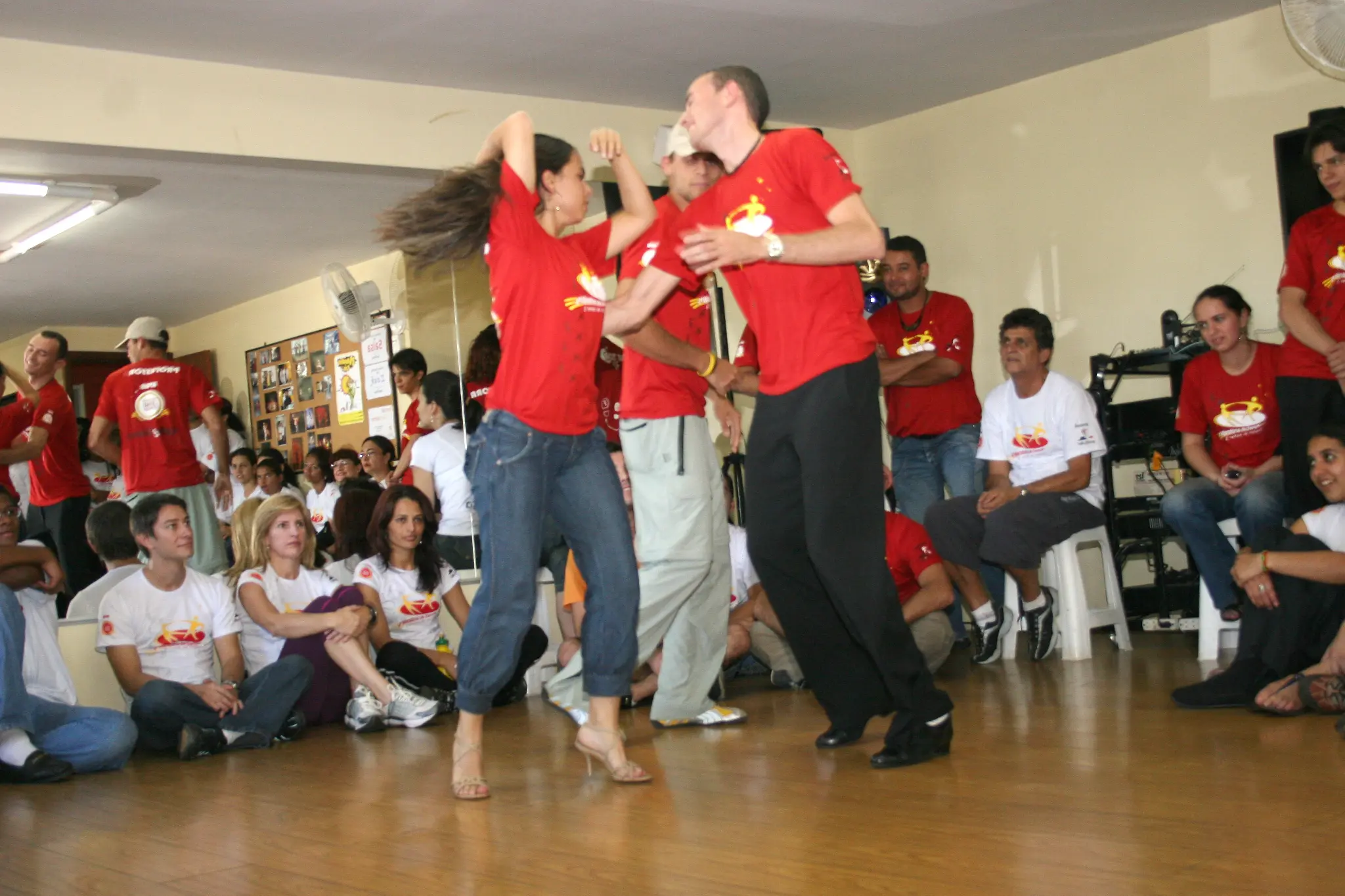Três participantes com camisetas vermelhas dançam diante do público